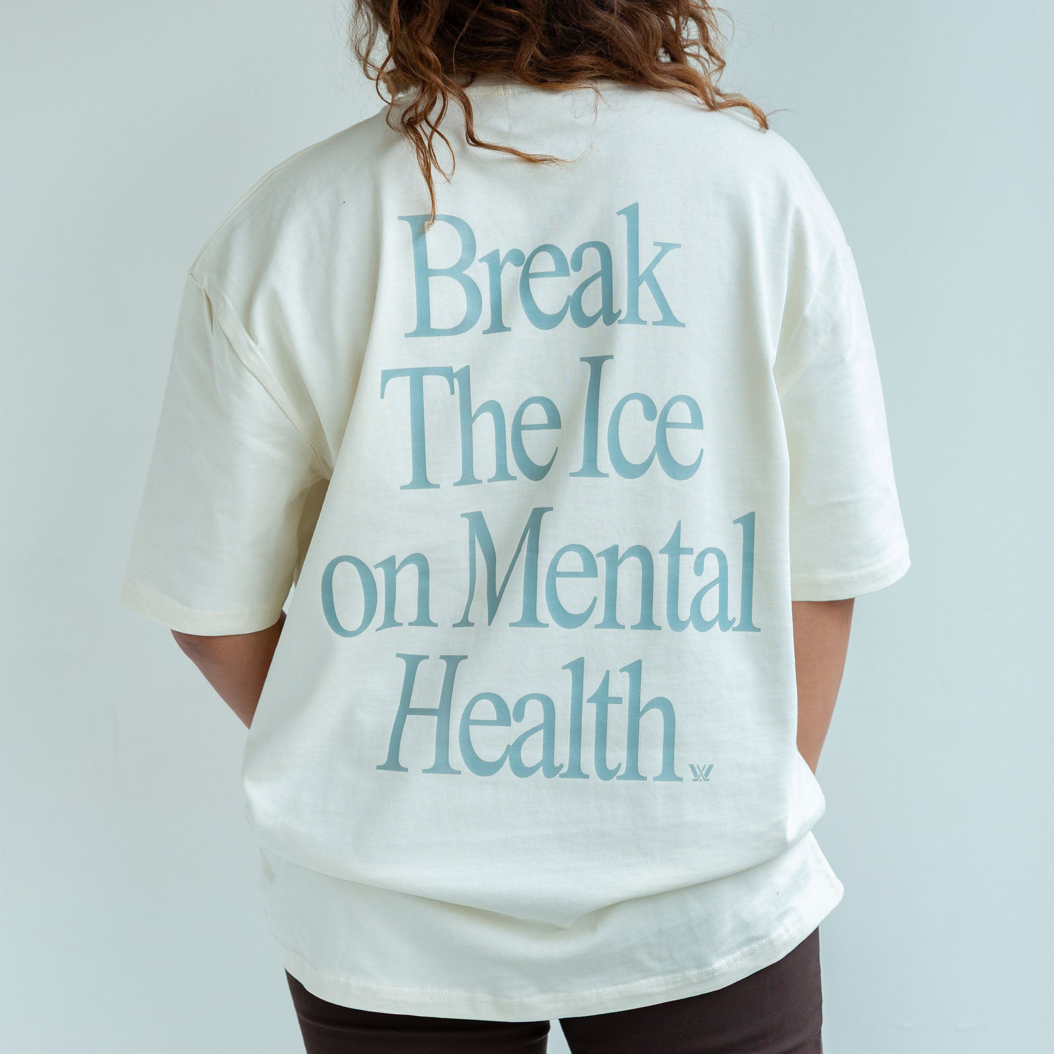 Person wearing a white t-shirt with 'Break The Ice on Mental Health' text on the back against a light gray background