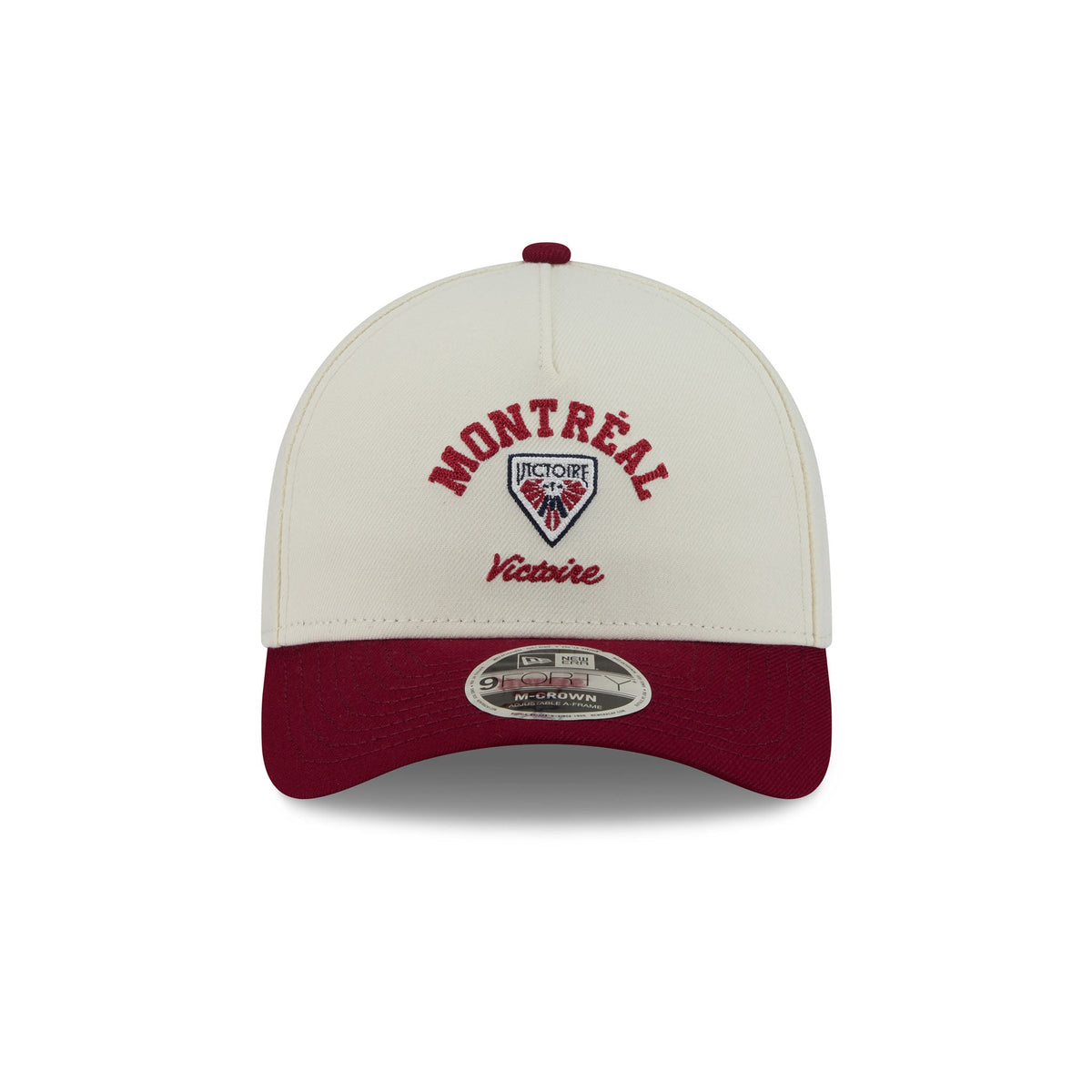 A structured baseball cap with an off-white crown and a dark maroon visor, featuring embroidered 'MONTREAL Victoire' text and a shield logo on the front. A silver sticker is visible at the front edge.