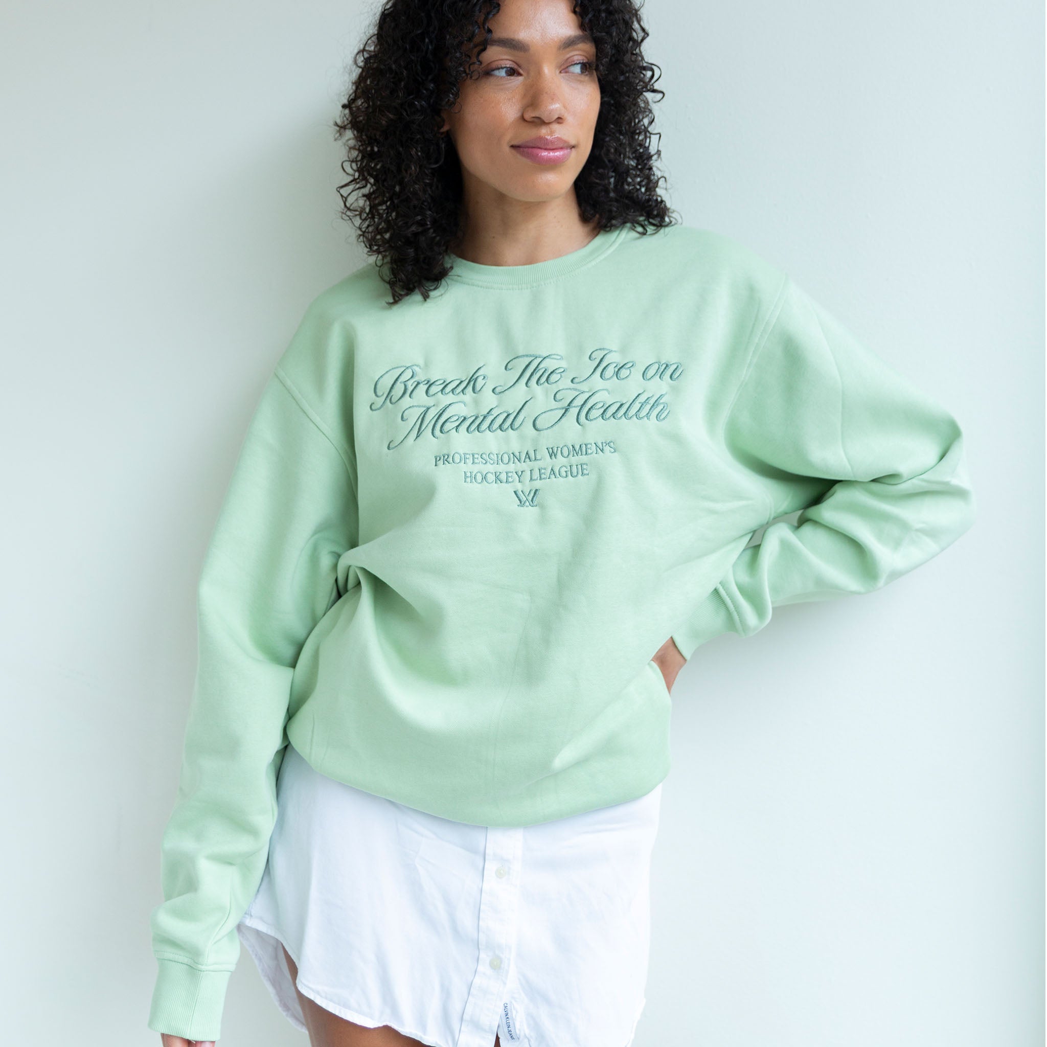 Person wearing a light green sweatshirt with text, standing against a plain background