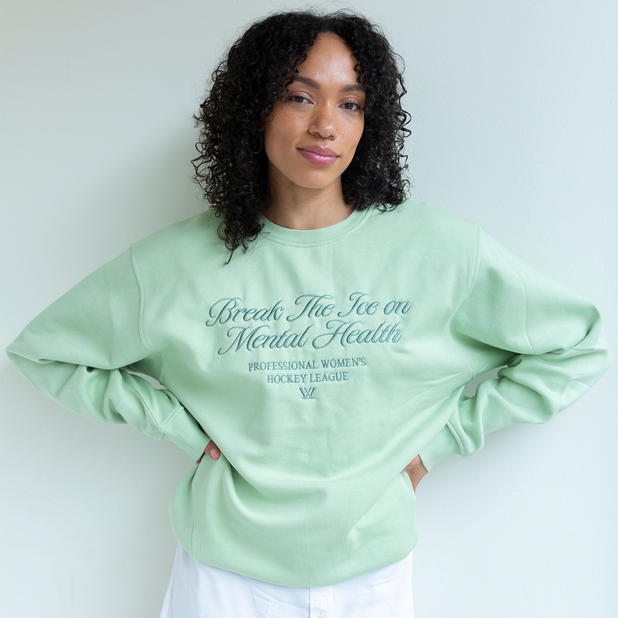 Person wearing a light green sweatshirt with text, standing against a plain background