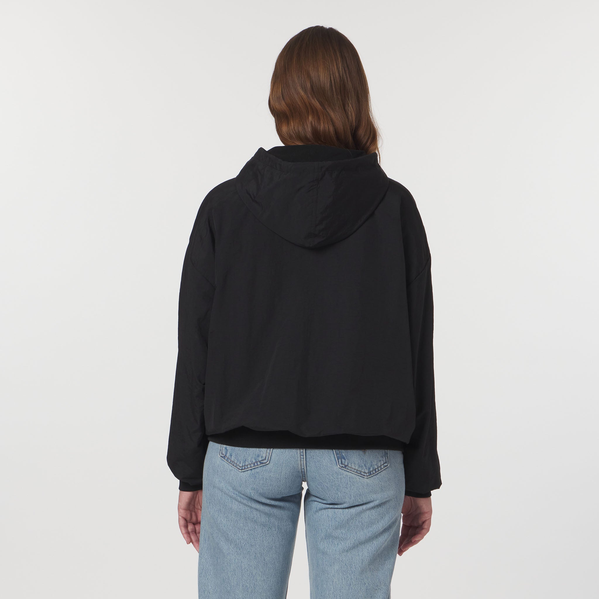 Person wearing a black hoodie and light blue jeans on a white background