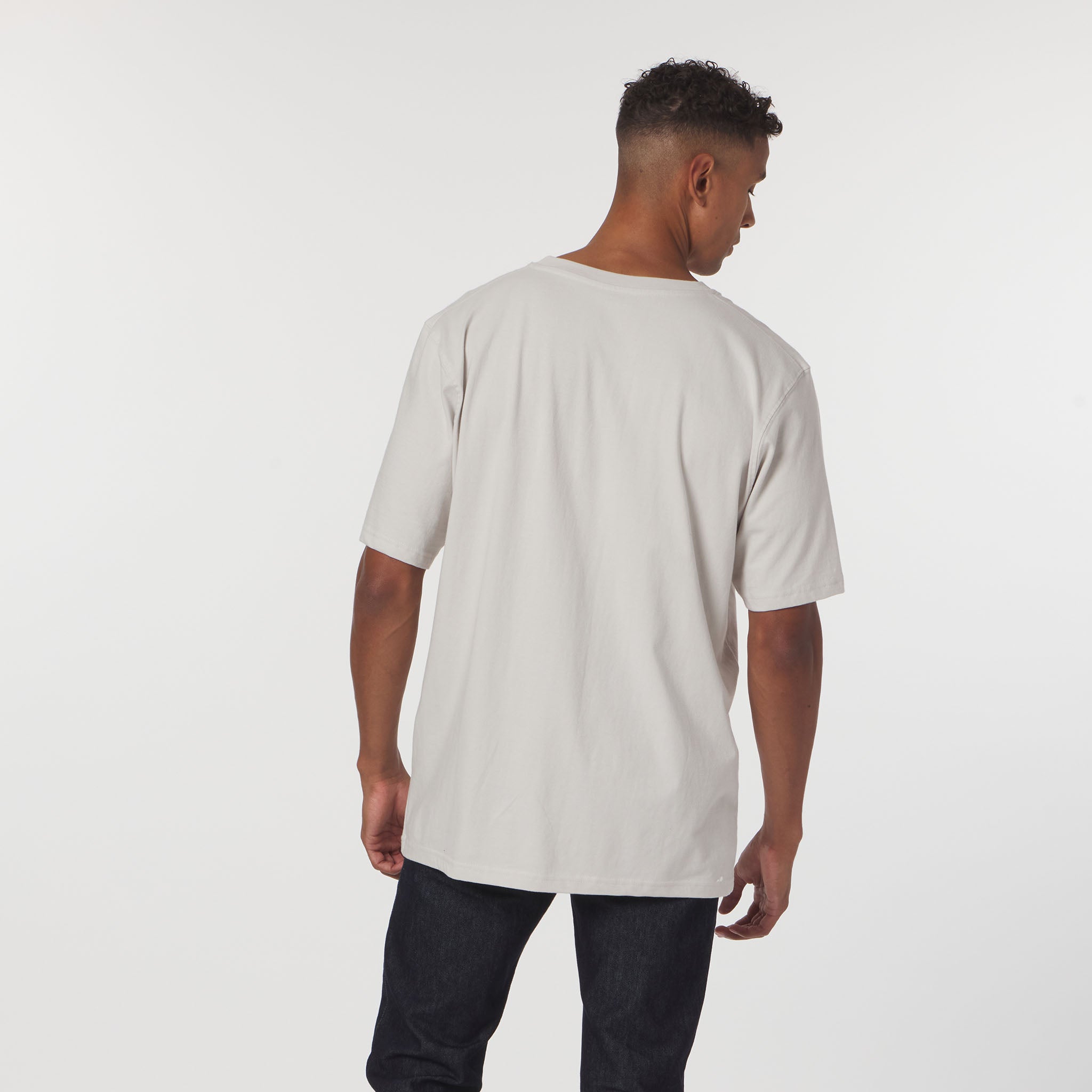 Man wearing a beige t-shirt and dark pants on a white background