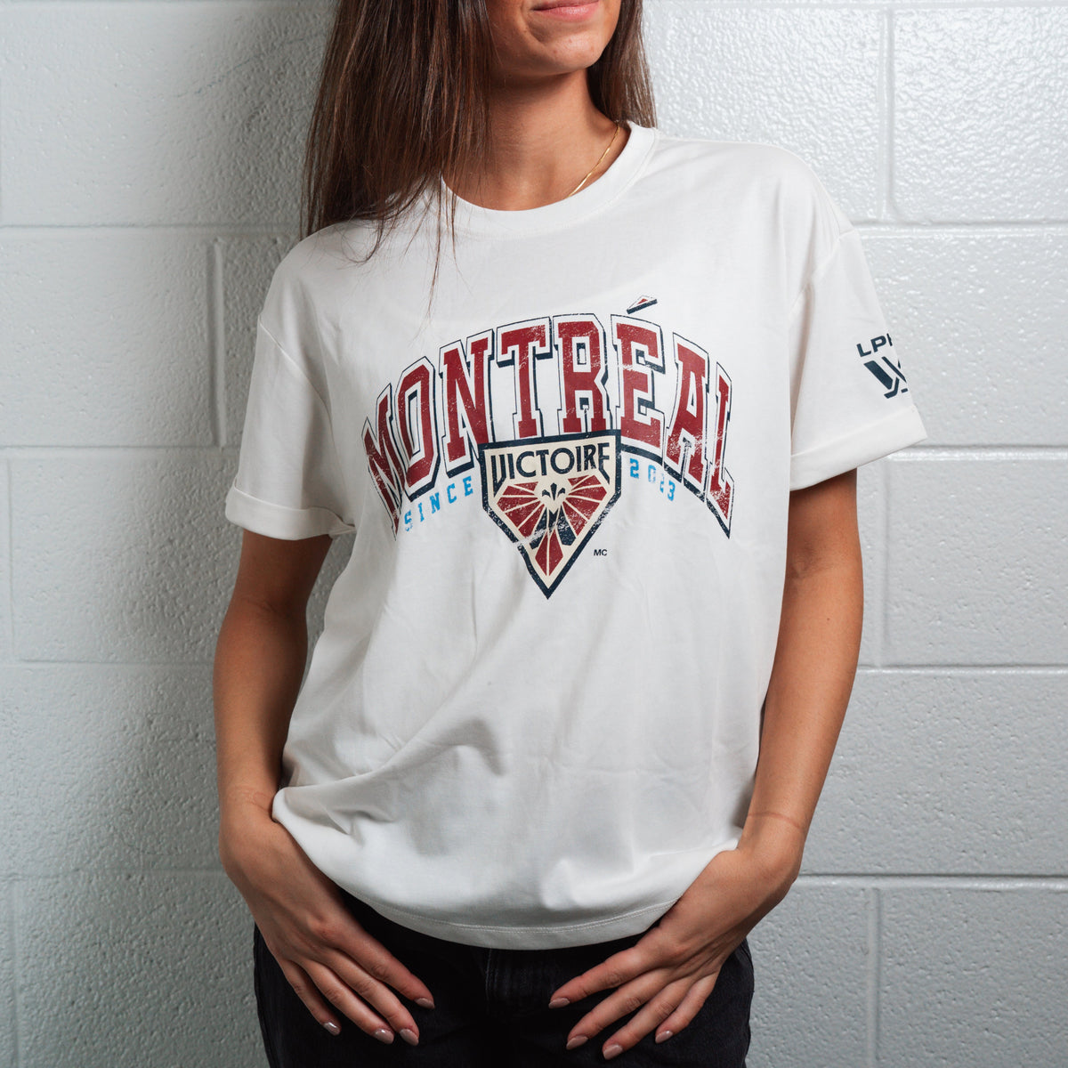 Person wearing a white t-shirt with 'Montreal' and 'Victoire' text against a white brick wall.