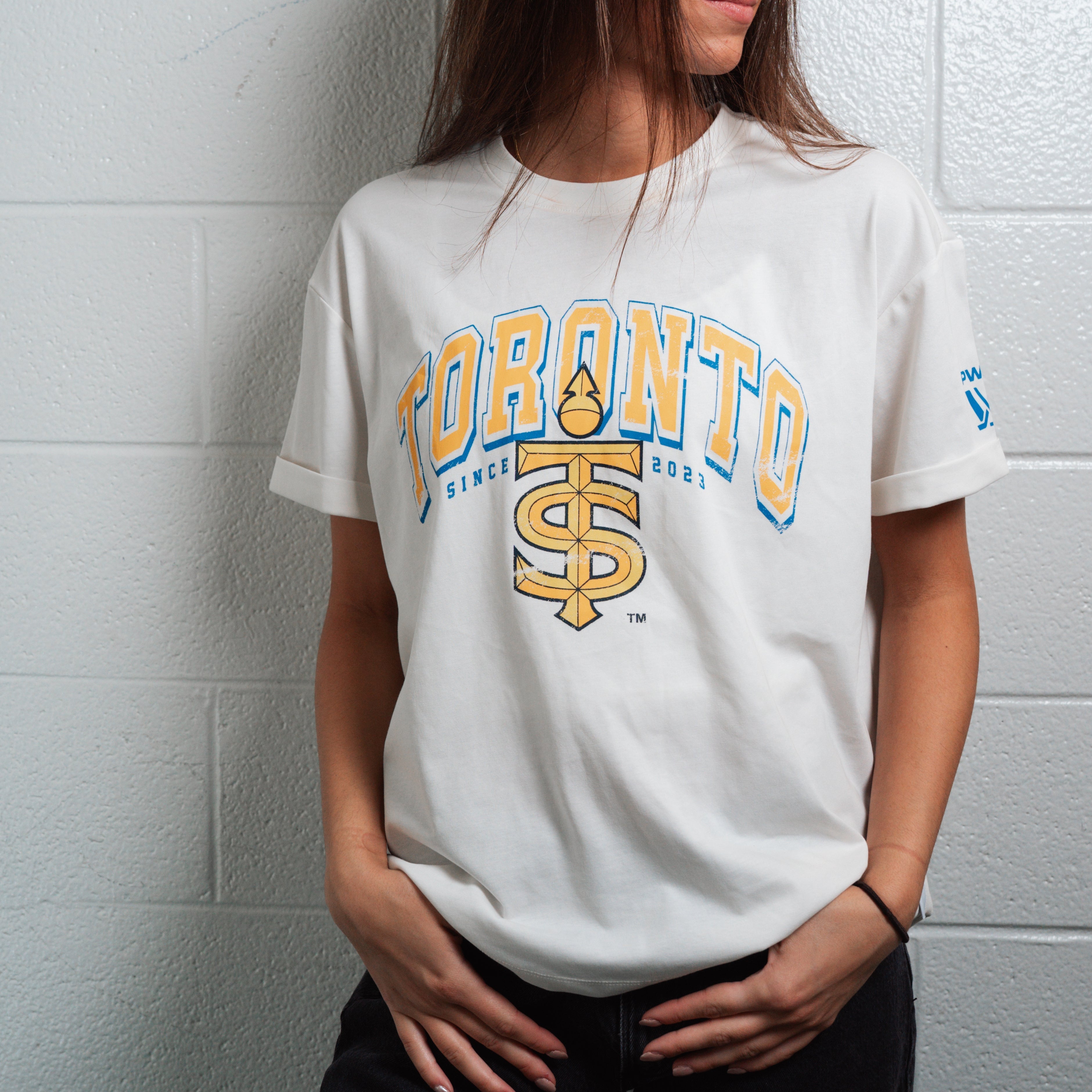 Person wearing a white t-shirt with 'Toronto' and logo against a light gray wall