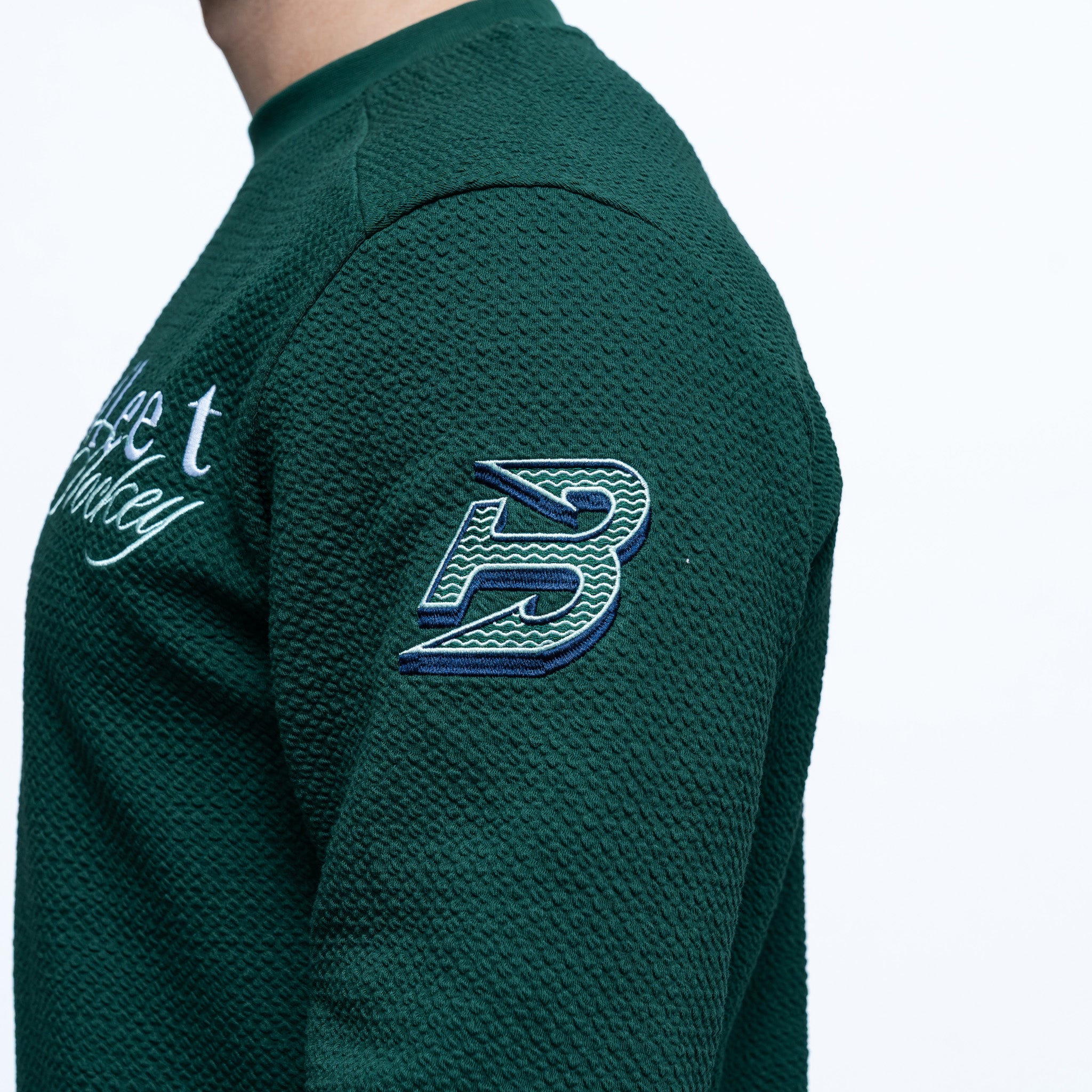 Green textured sweater with a logo on the sleeve against a white background