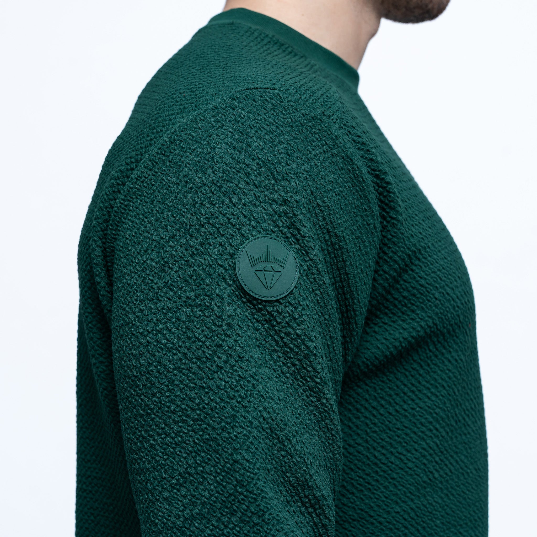 Green textured sweater with a logo patch on a white background