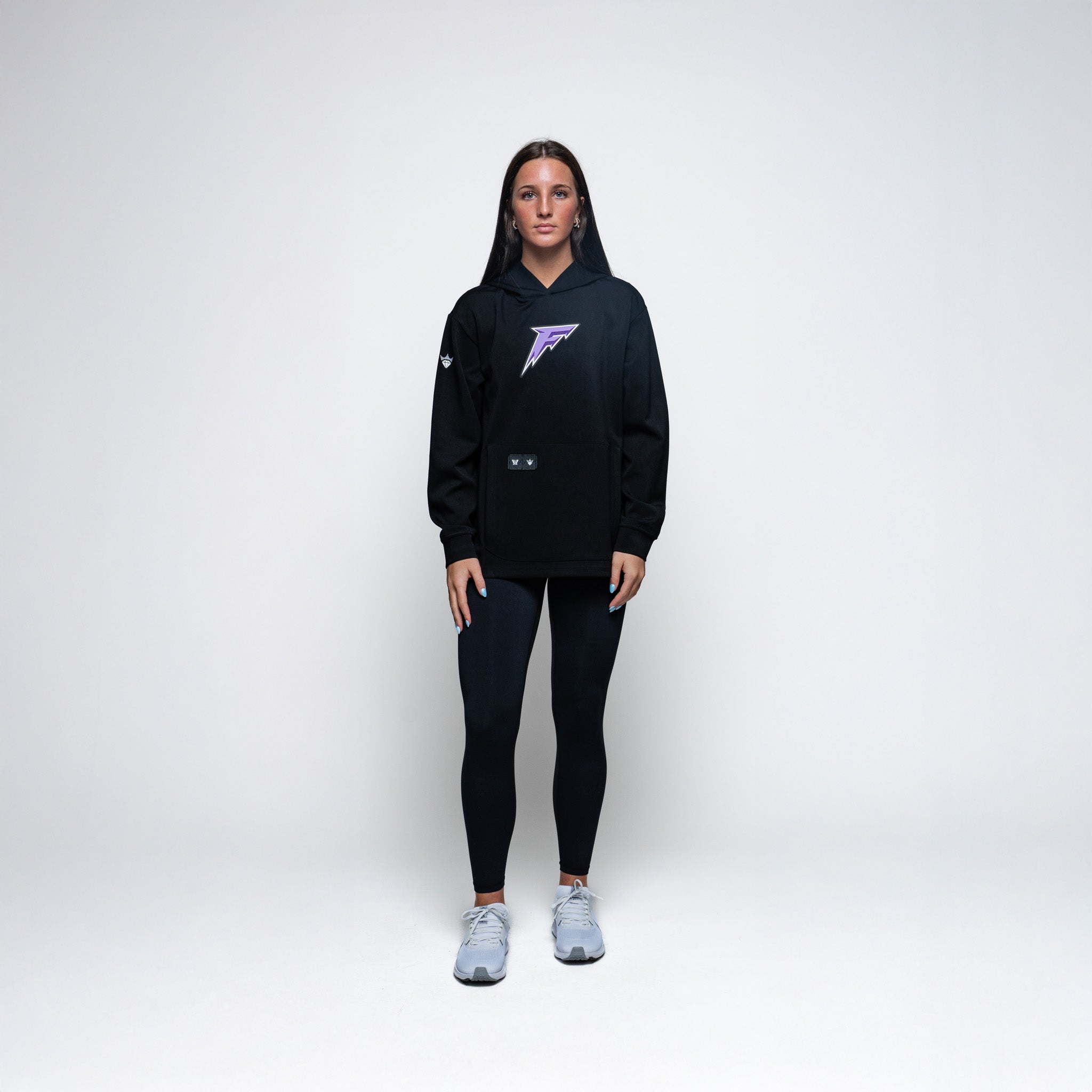 Person wearing a black hoodie with a logo and black leggings on a white background
