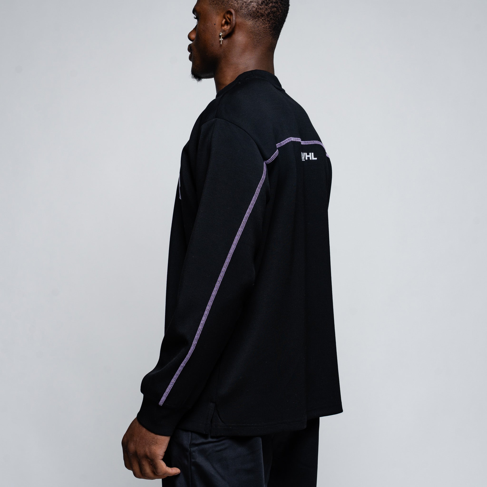 Person wearing a black long-sleeve shirt with a logo on the sleeve against a gray background