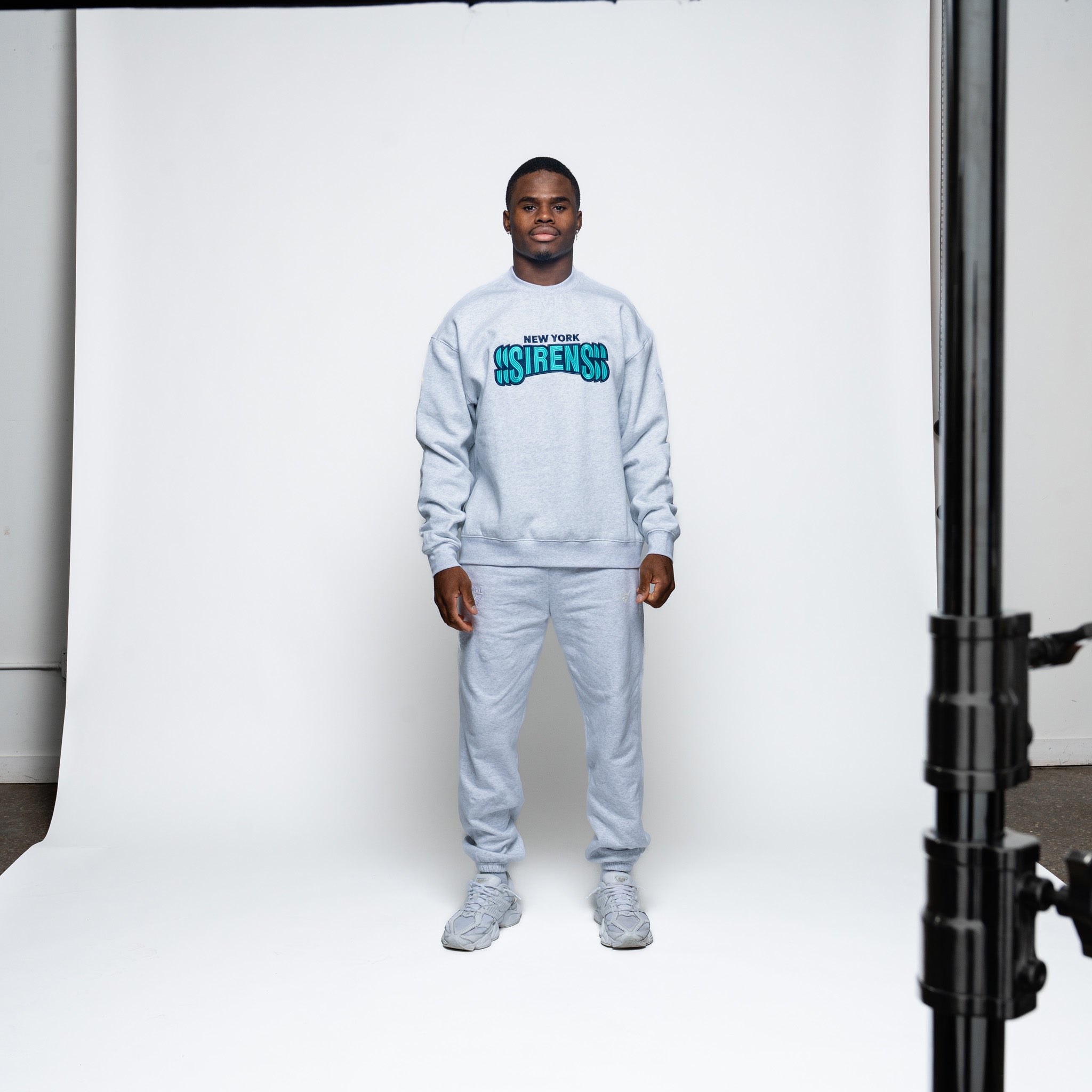 Person wearing a gray sweatshirt and pants set with visible branding in a studio setting.