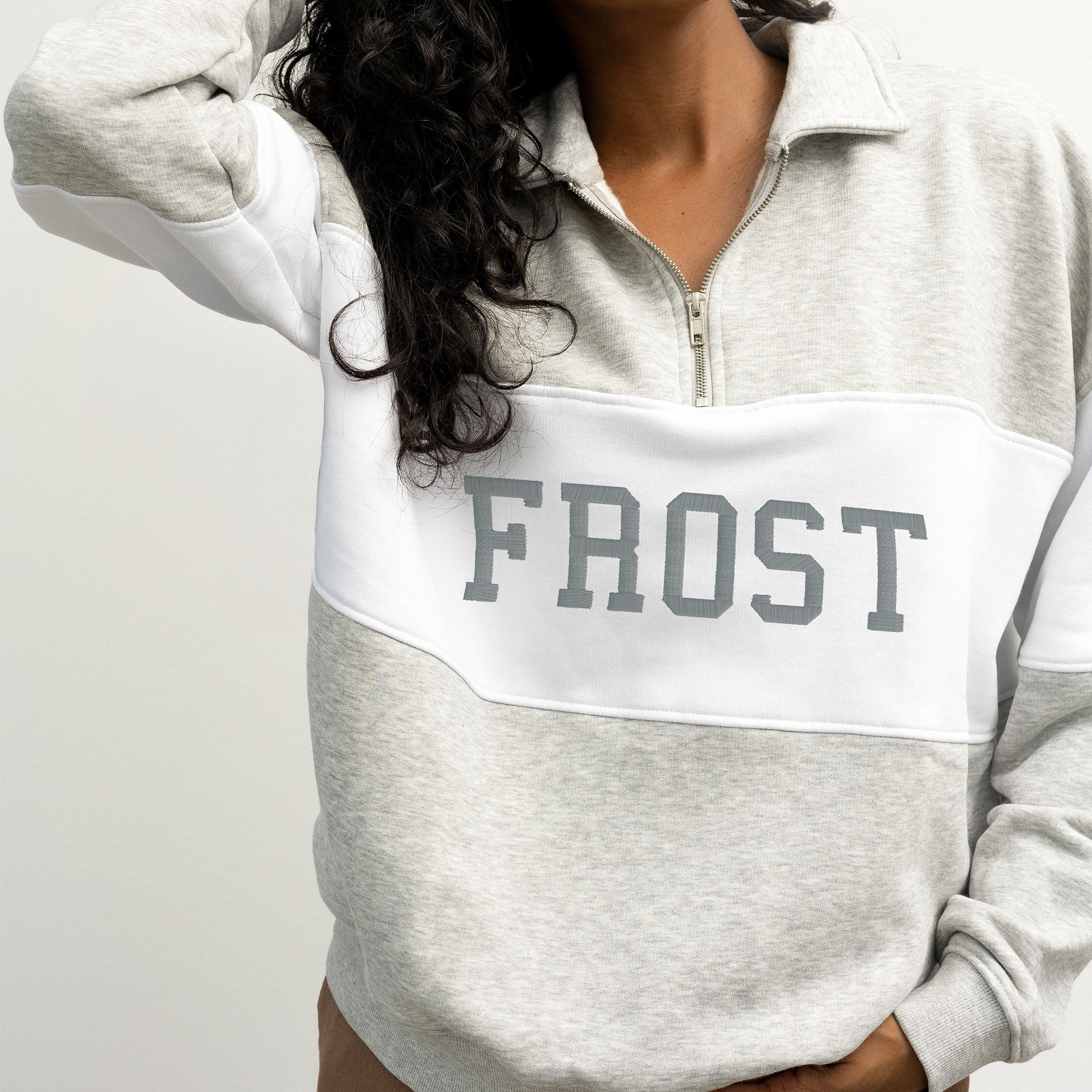 Person wearing a gray and white pullover with 'FROST' text on a plain background