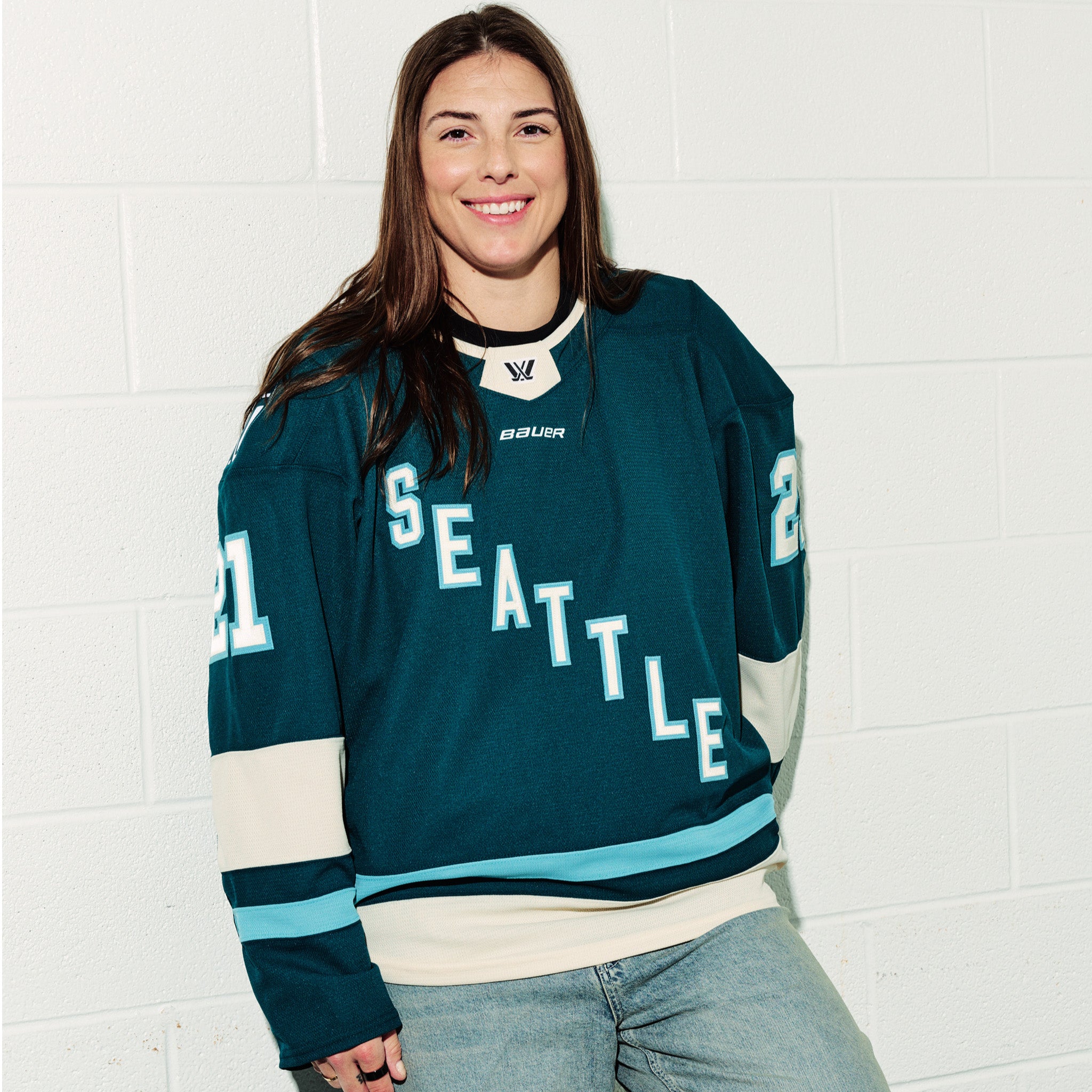 Hilary Knight wearing her green PWHL Seattle jersey with, standing against a white tiled wall.