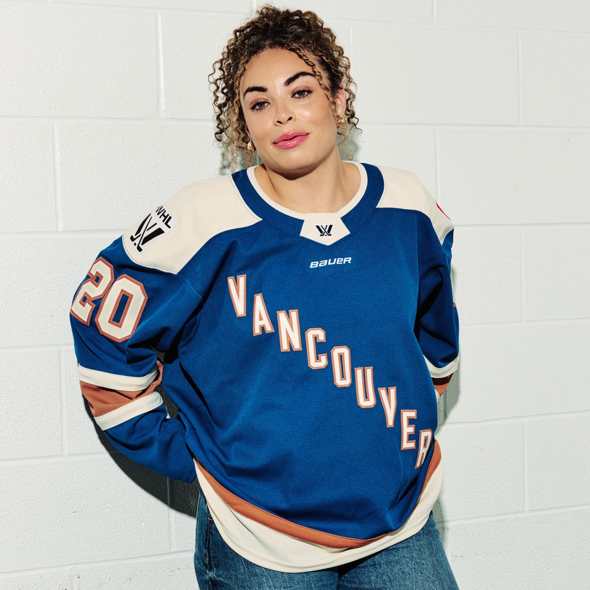 Sarah Nurse wearing her blue PWHL Vancouver jersey with, standing against a white tiled wall.