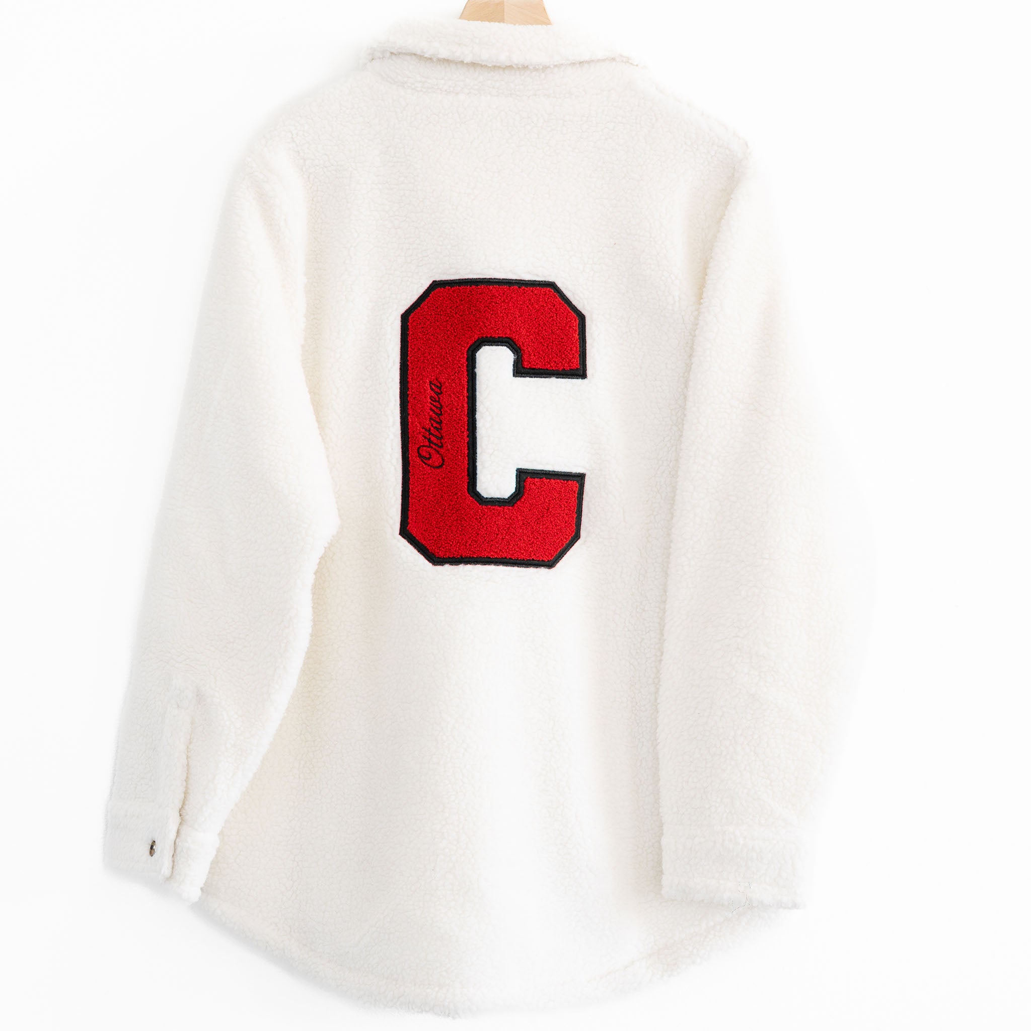 The back of a White Sherpa Jacket with a red C that says Ottawa inside it