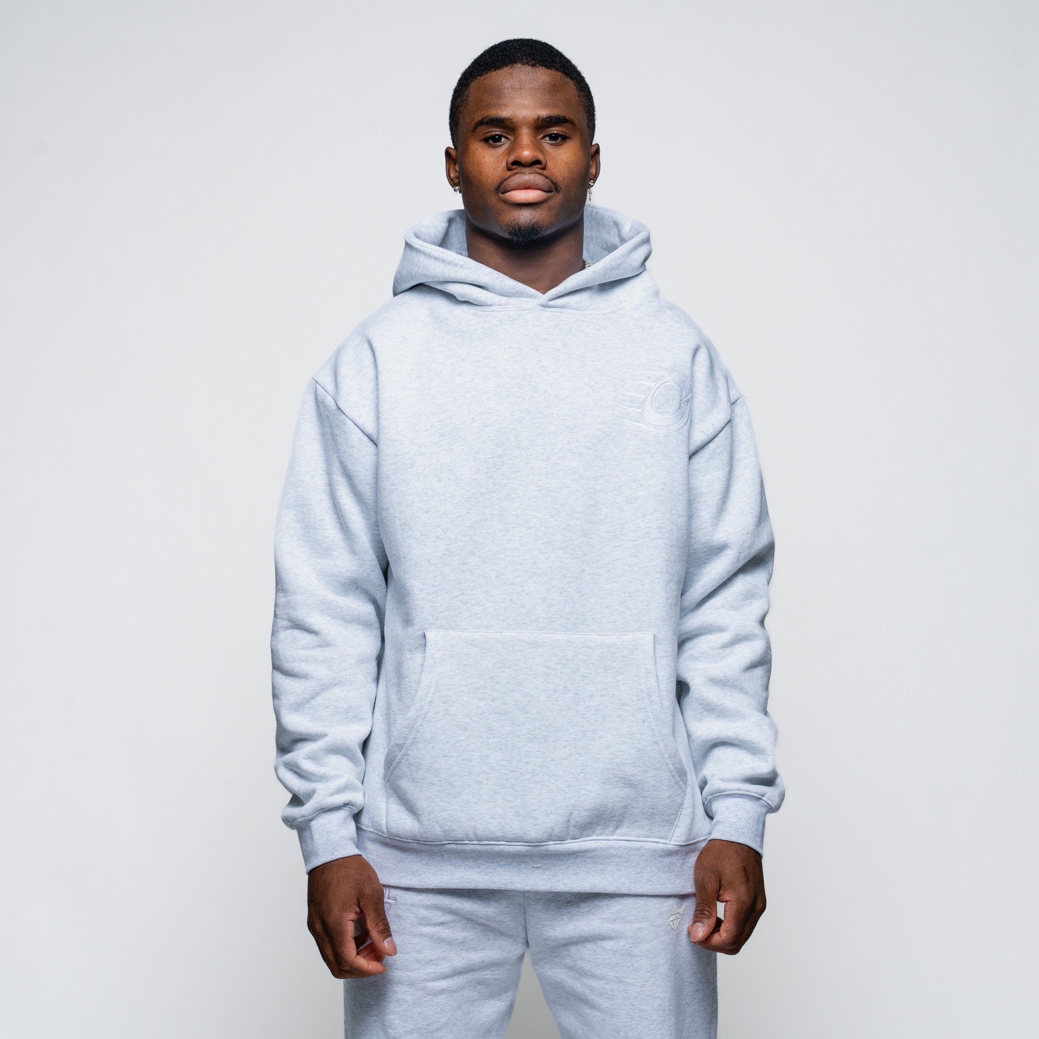 Man wearing a light gray hoodie and pants on a plain background