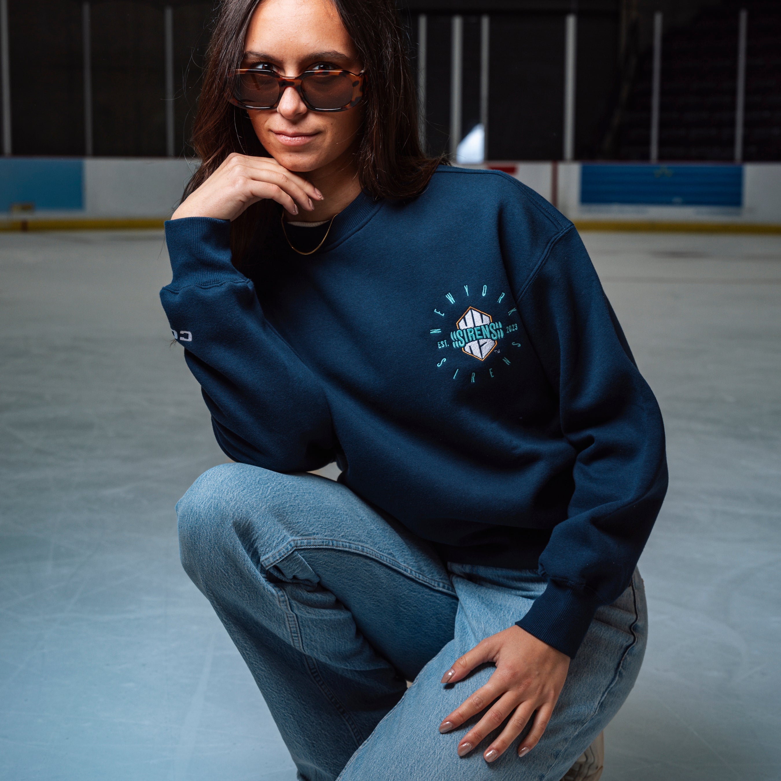 Person wearing a blue sweatshirt with a logo, sitting on an ice rink.