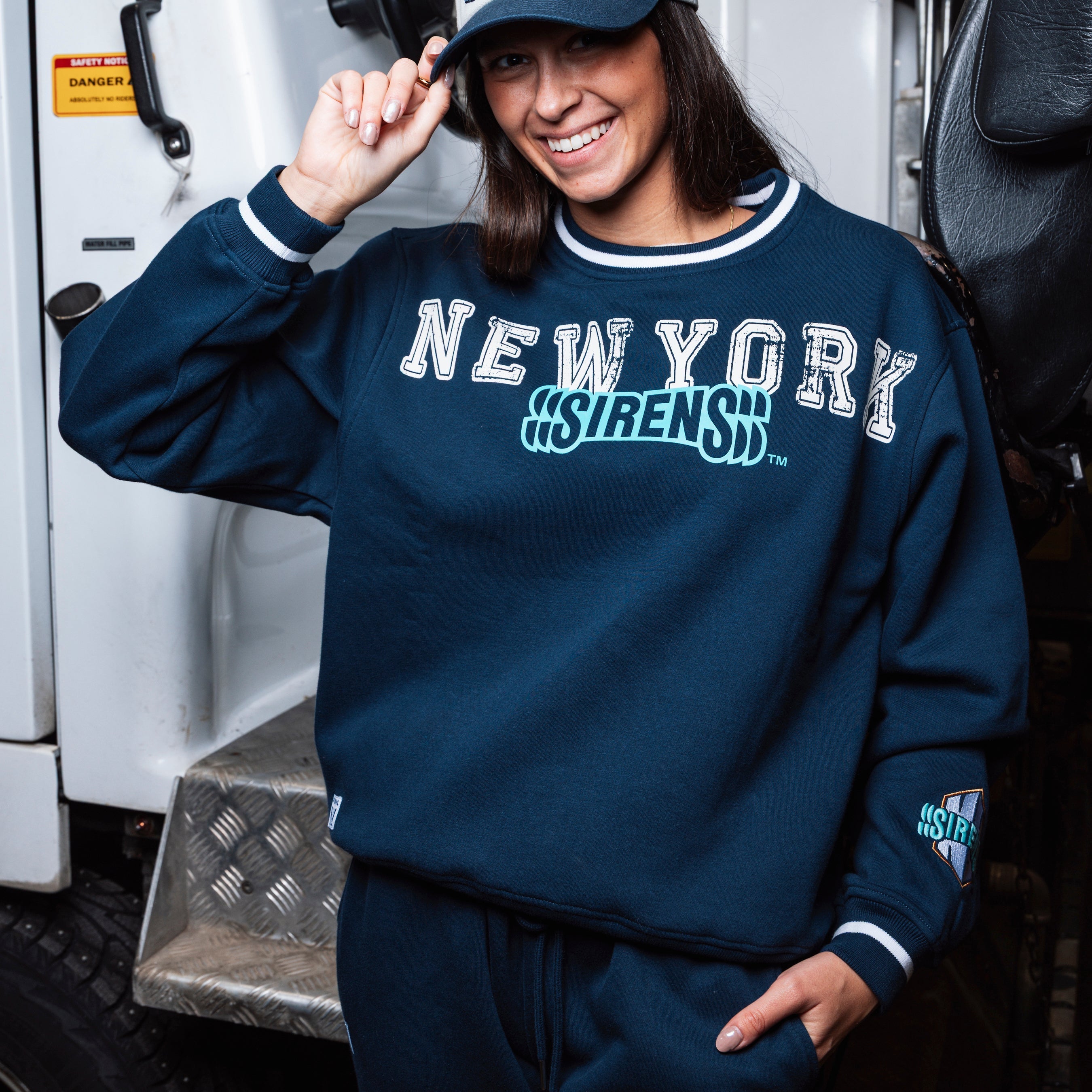 Person wearing a navy blue sweatshirt with 'New York Sirens' text, standing next to a vehicle.