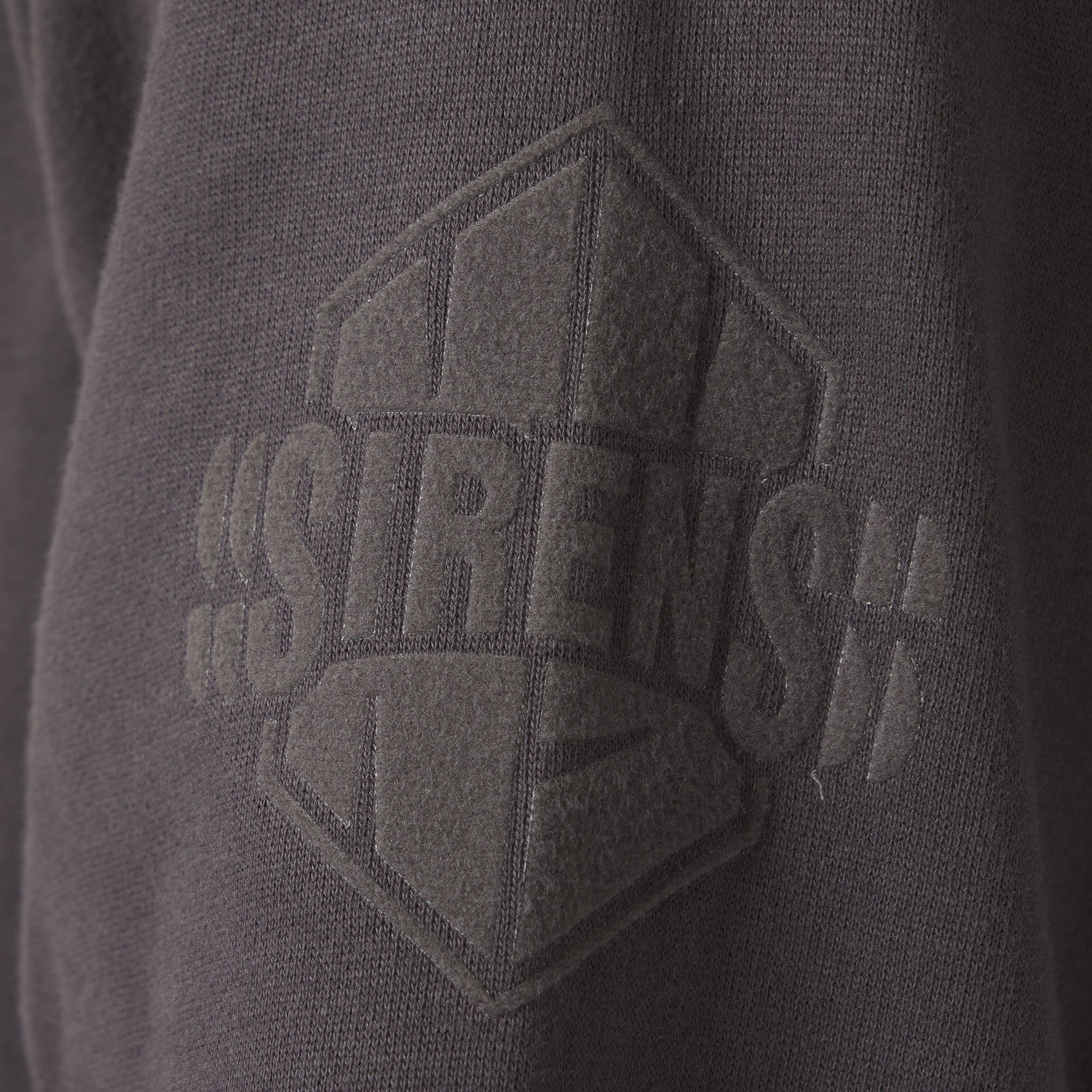 Close-up of a dark gray hoodie with a textured logo on the chest.