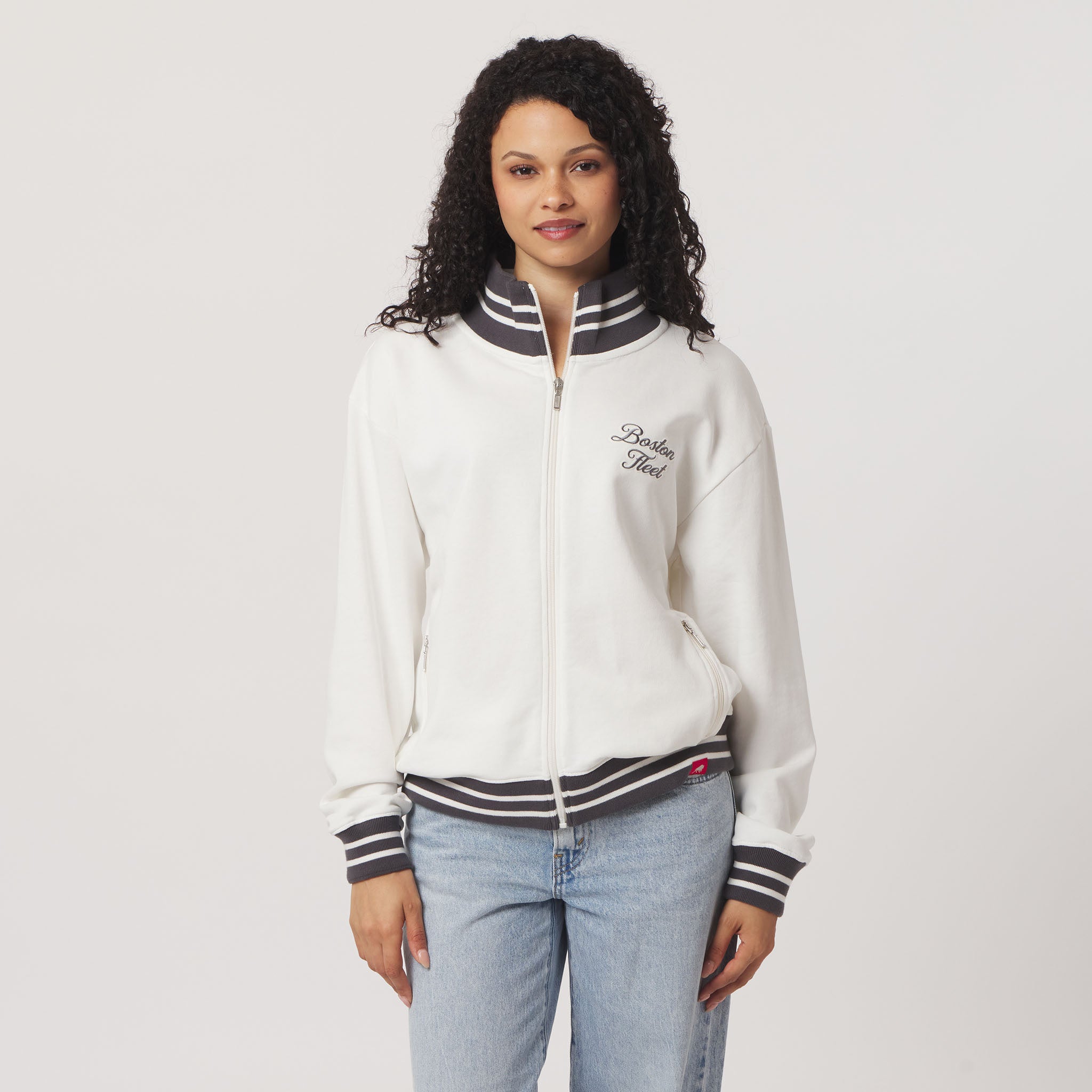 Woman wearing a white jacket with black accents and blue jeans on a plain background