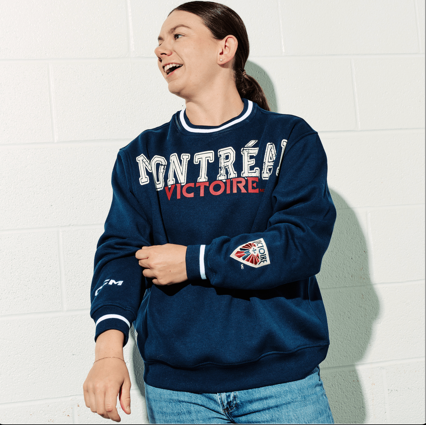 Person wearing a navy blue sweatshirt with 'Montreéal Victoire' text against a white brick wall.