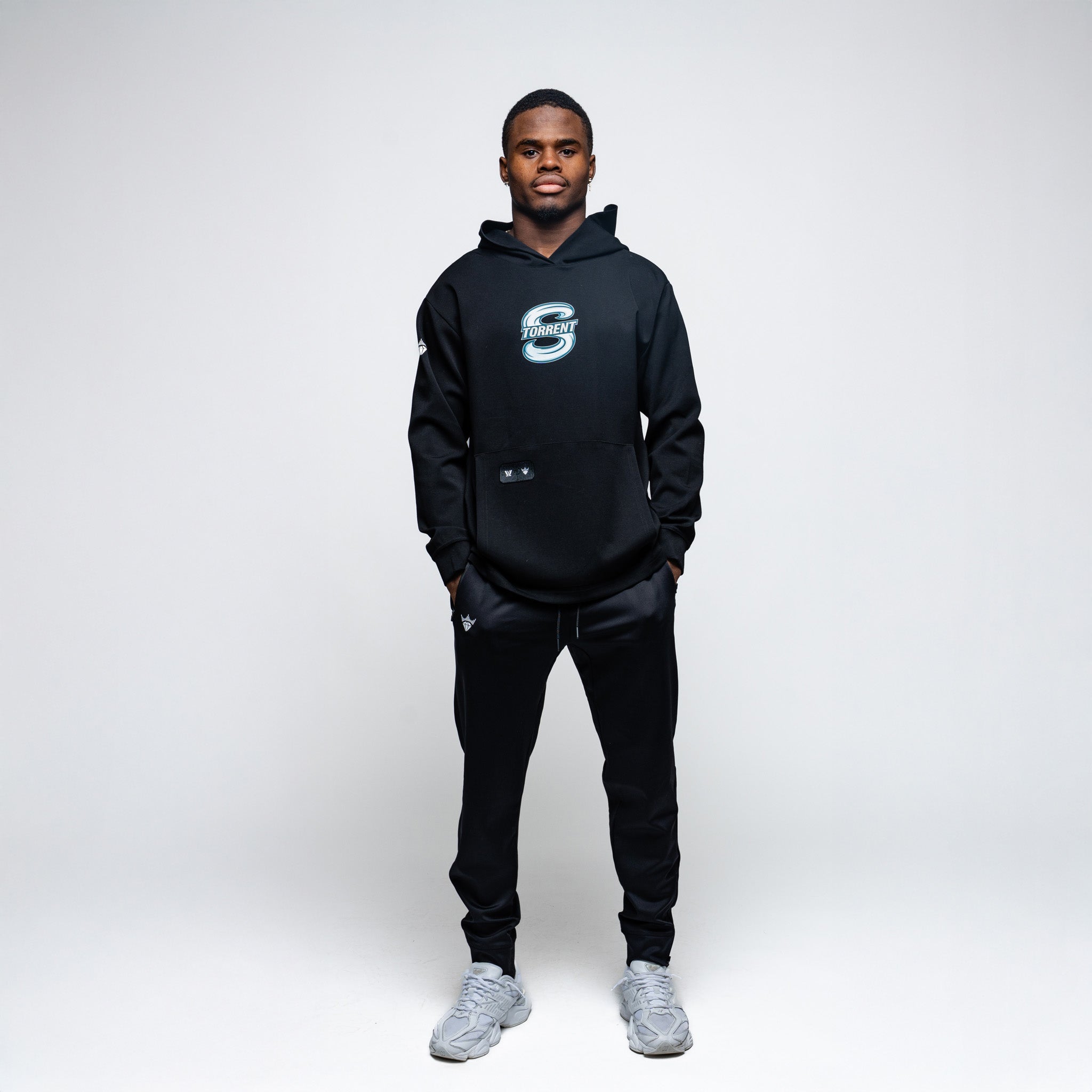 Man wearing a black hoodie and pants with a logo on a white background