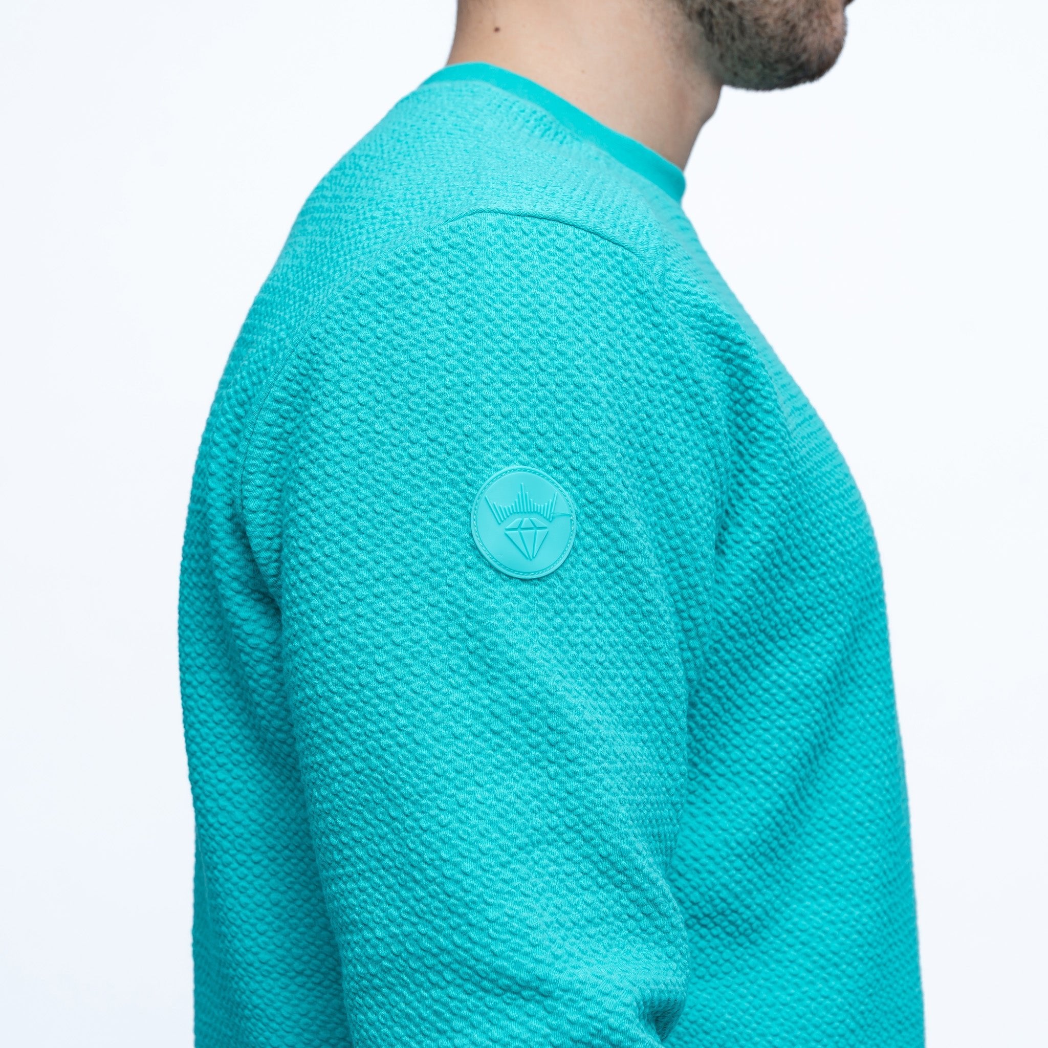 Teal sweater with a logo on the chest against a white background