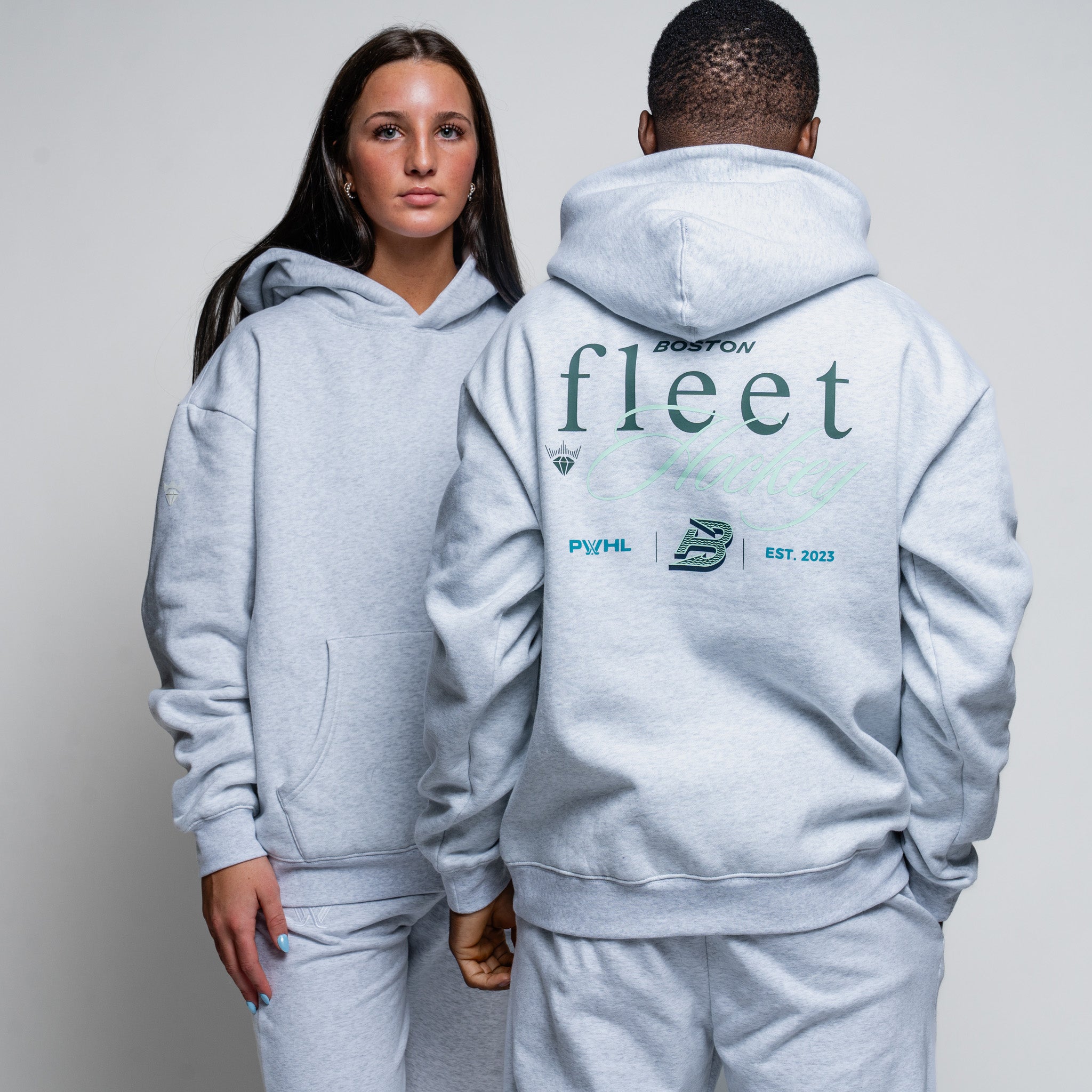 Two people wearing gray hoodies with 'fleet' branding on a plain background