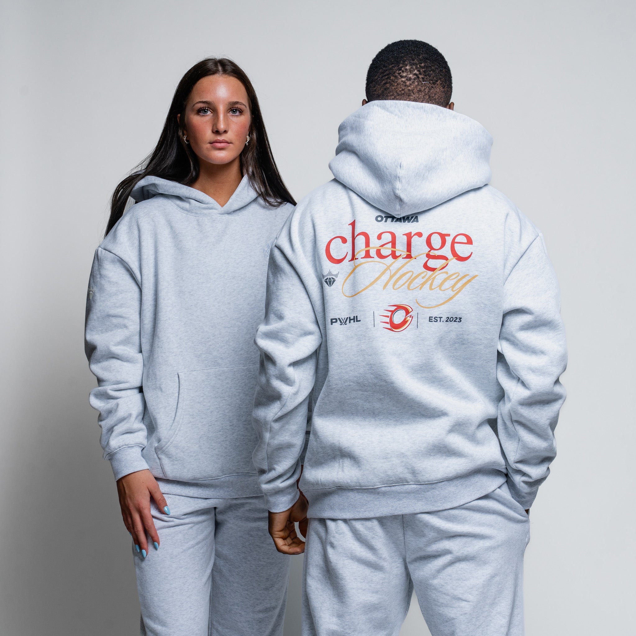 Two people wearing matching gray hoodies with branding on a plain background
