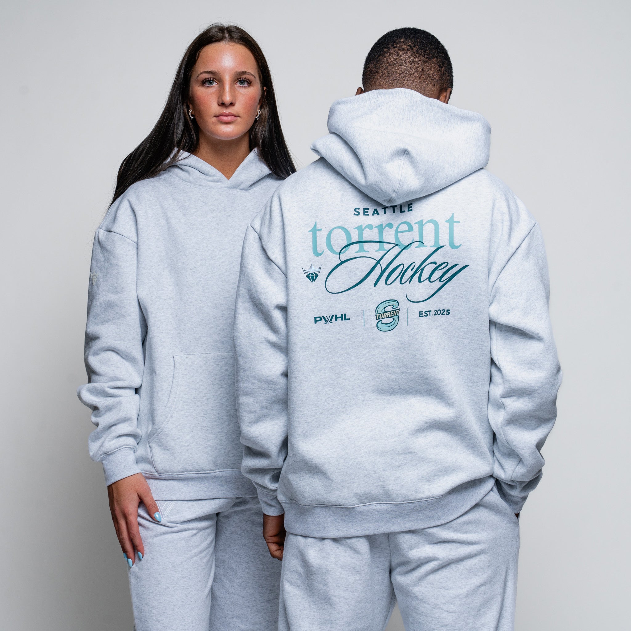 Two people wearing gray hoodies with 'Seattle torrent Hockey' branding on a plain background