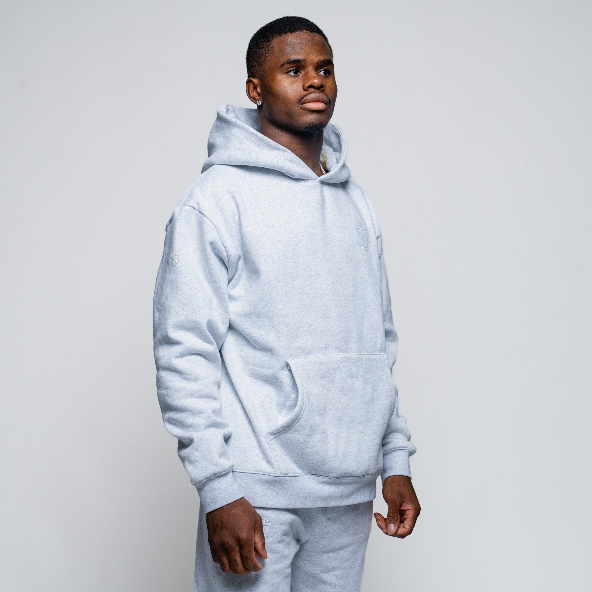 Man wearing a light gray hoodie and pants on a plain background