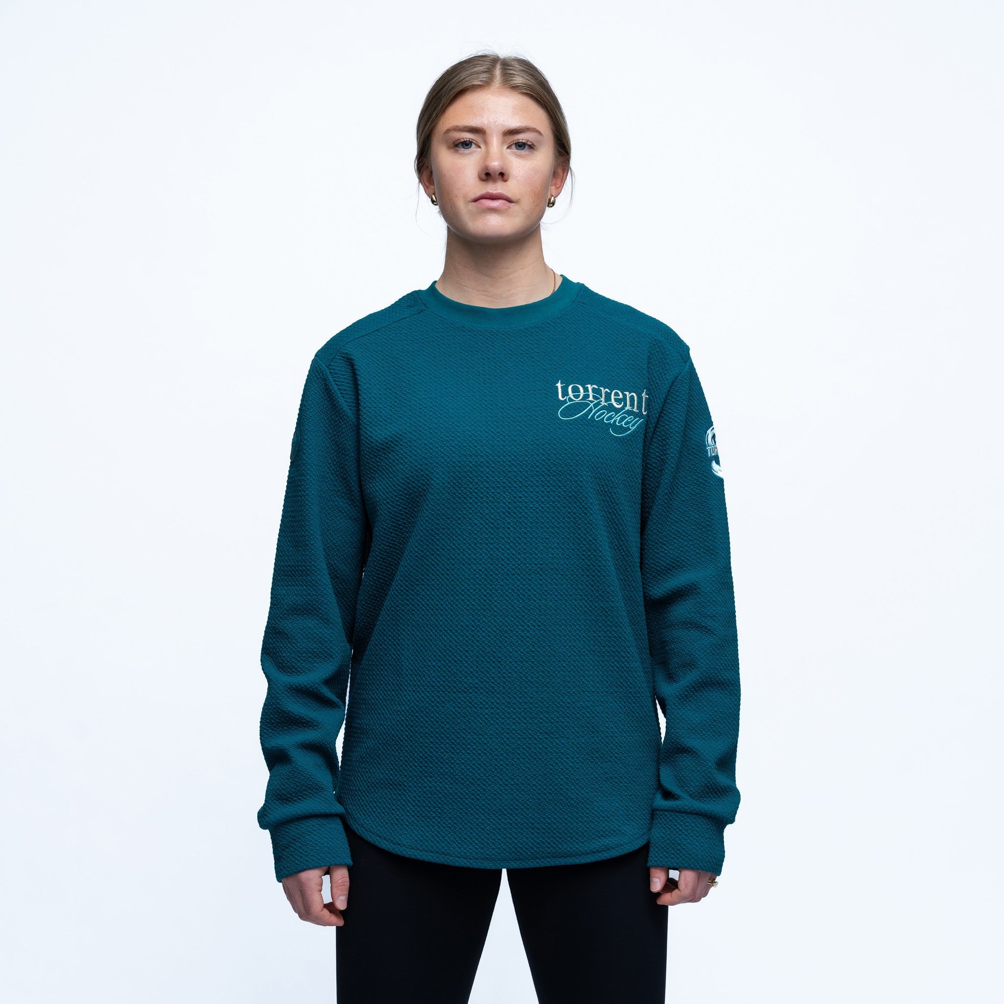 Person wearing a teal long-sleeve shirt with branding on a white background
