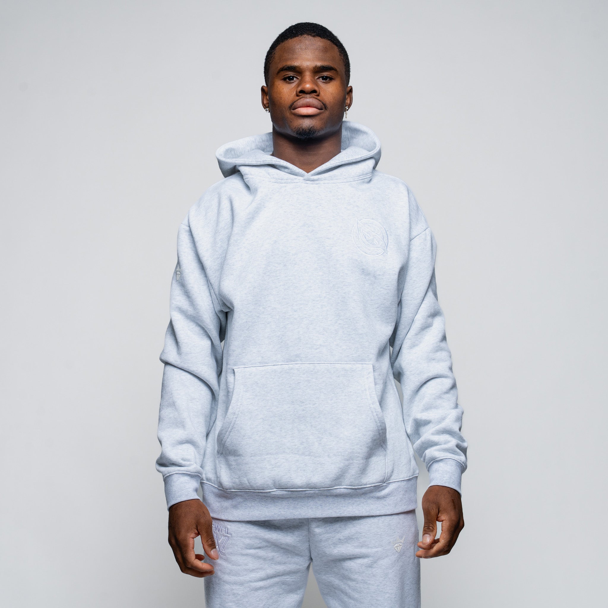 Man wearing a light gray hoodie and pants against a plain background