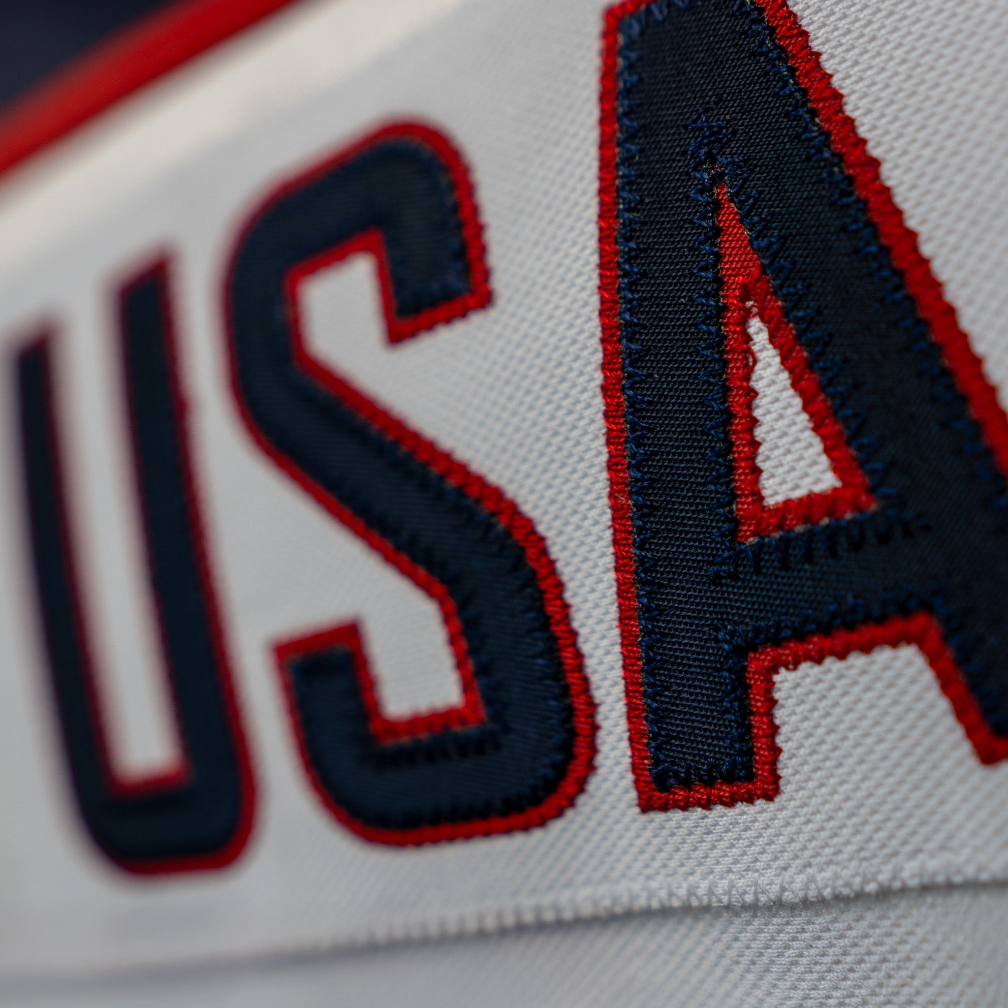 White name plate with 'USA' red stitching and navy letters on the white jersey.