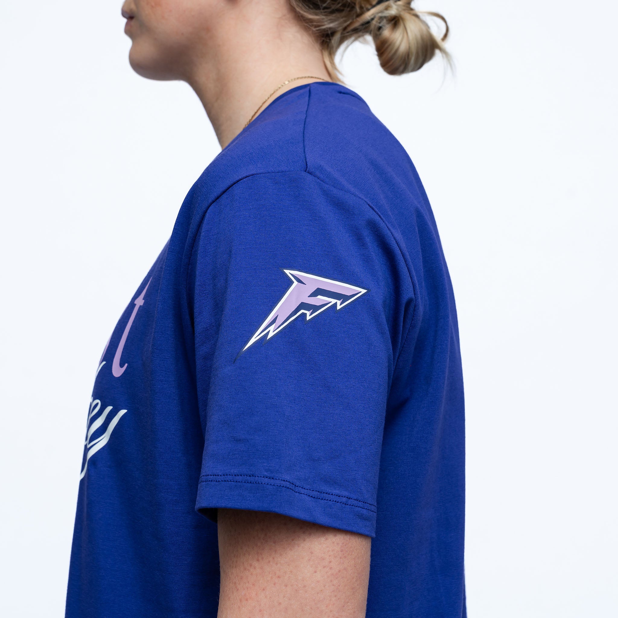 Person wearing a blue t-shirt with a logo on the sleeve against a white background