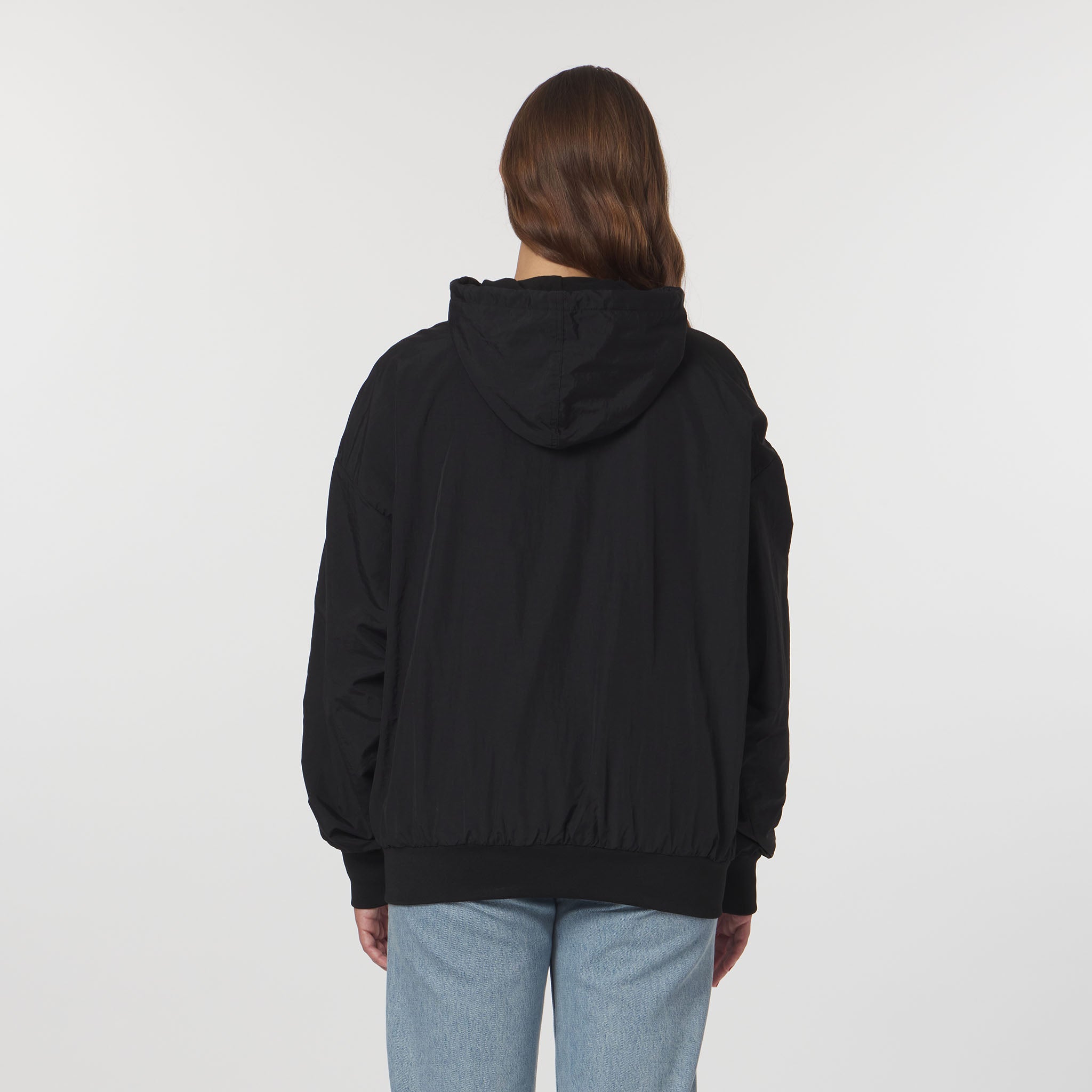 Person wearing a black hoodie and light blue jeans on a white background