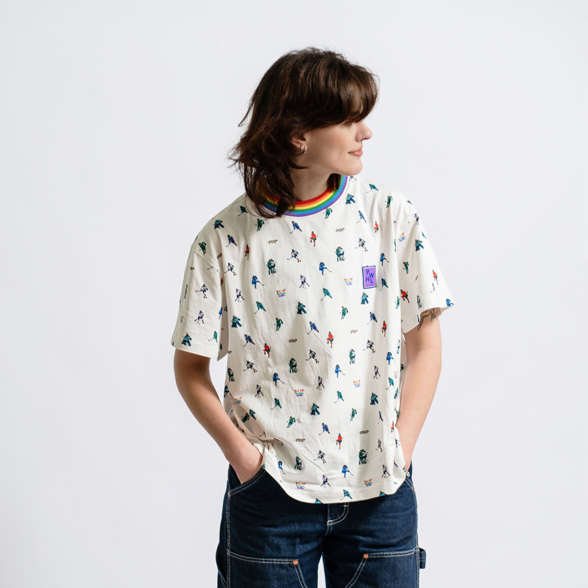 Person wearing a patterned t-shirt with a rainbow and logo on a plain background