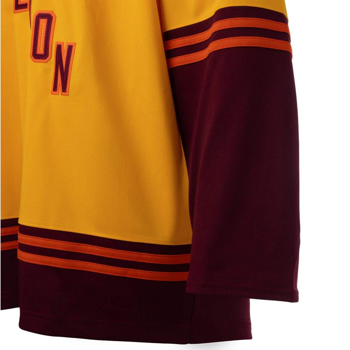 Front of a gold jersey with maroon color blocking on the sleeves and bottom hem with orange stipes on top. 'HAMILTON' is in maroon with orange outlining diagonally across the chest. 