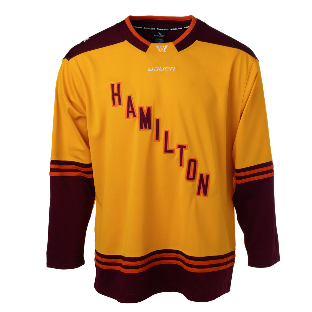 Front of a gold jersey with maroon shoulder caps. Maroon color blocking on the sleeves and bottom hem with orange stipes on top. 'HAMILTON' is in maroon with orange outlining diagonally across the chest. The collar is maroon with orange trim and a gold color block in front showcasing a white PWHL logo with a Bauer logo below it. 