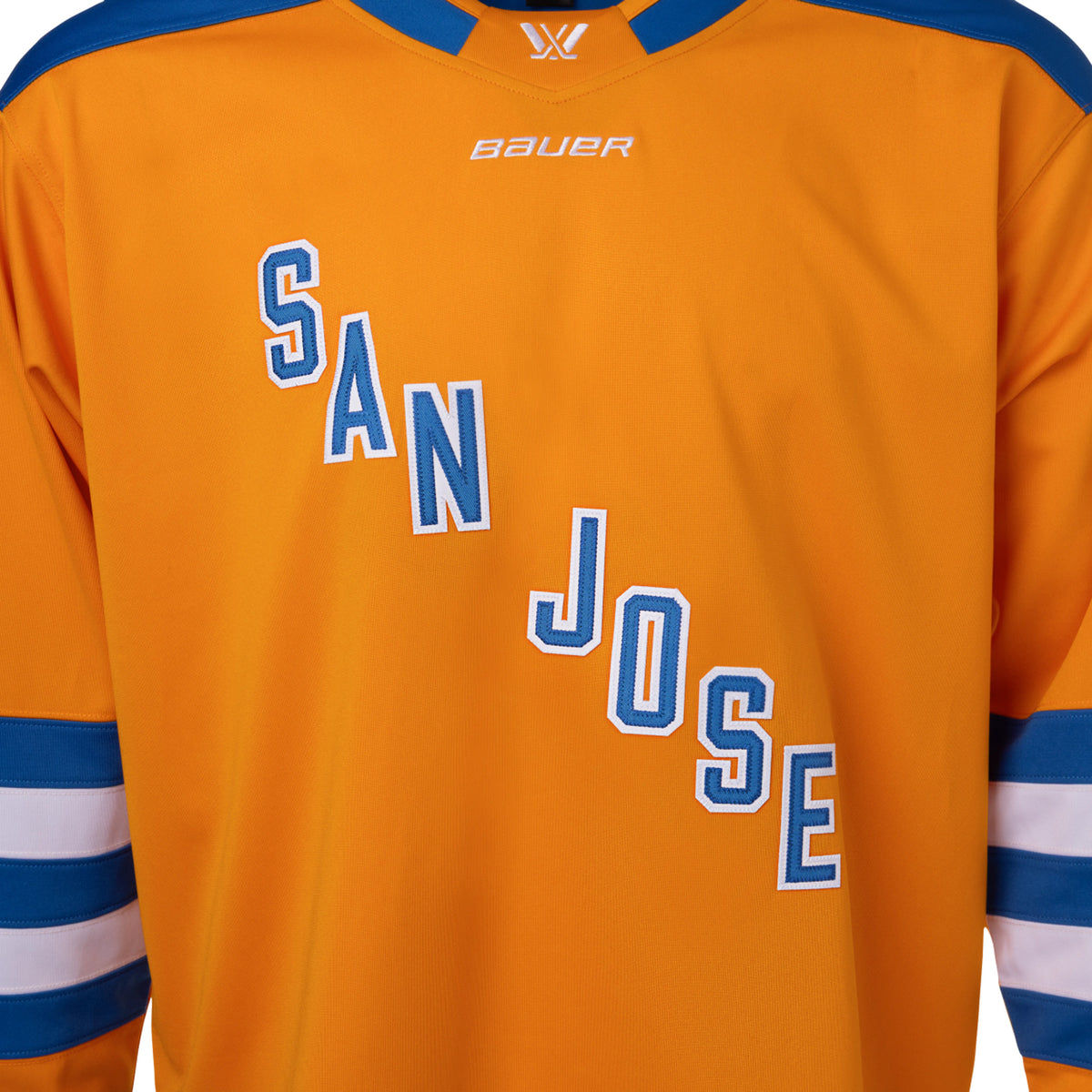 Front of an orange jersey with blue shoulder caps and blue and white stripes along the sleeves and bottom hem. In blue with white outlining is 'SAN JOSE' diagonally across the chest. The collar is blue with orange trim and color blocking on the front to showcase a white PWHL logo and a white Bauer logo below it. 