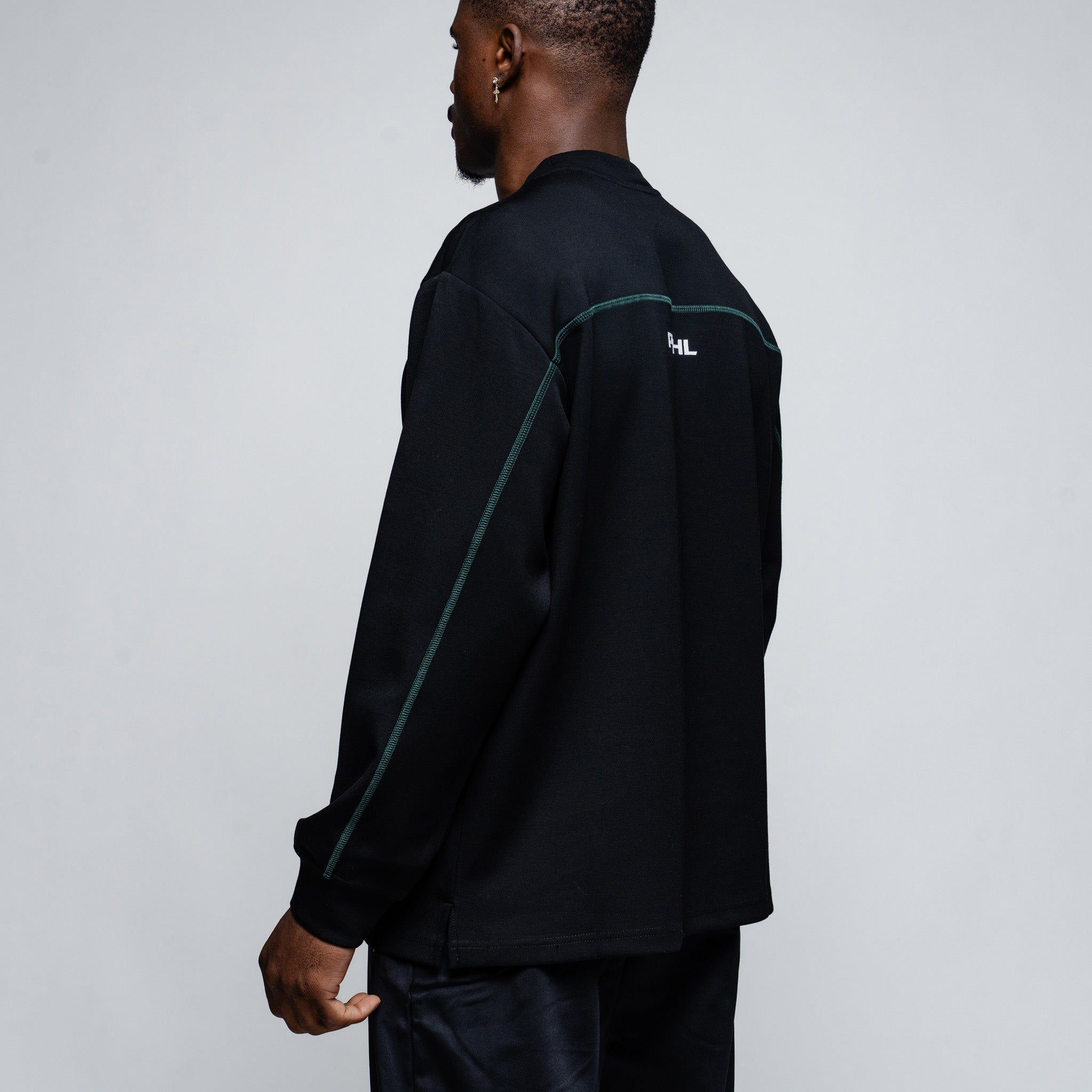 Person wearing a black long-sleeve shirt with green accents on a plain background