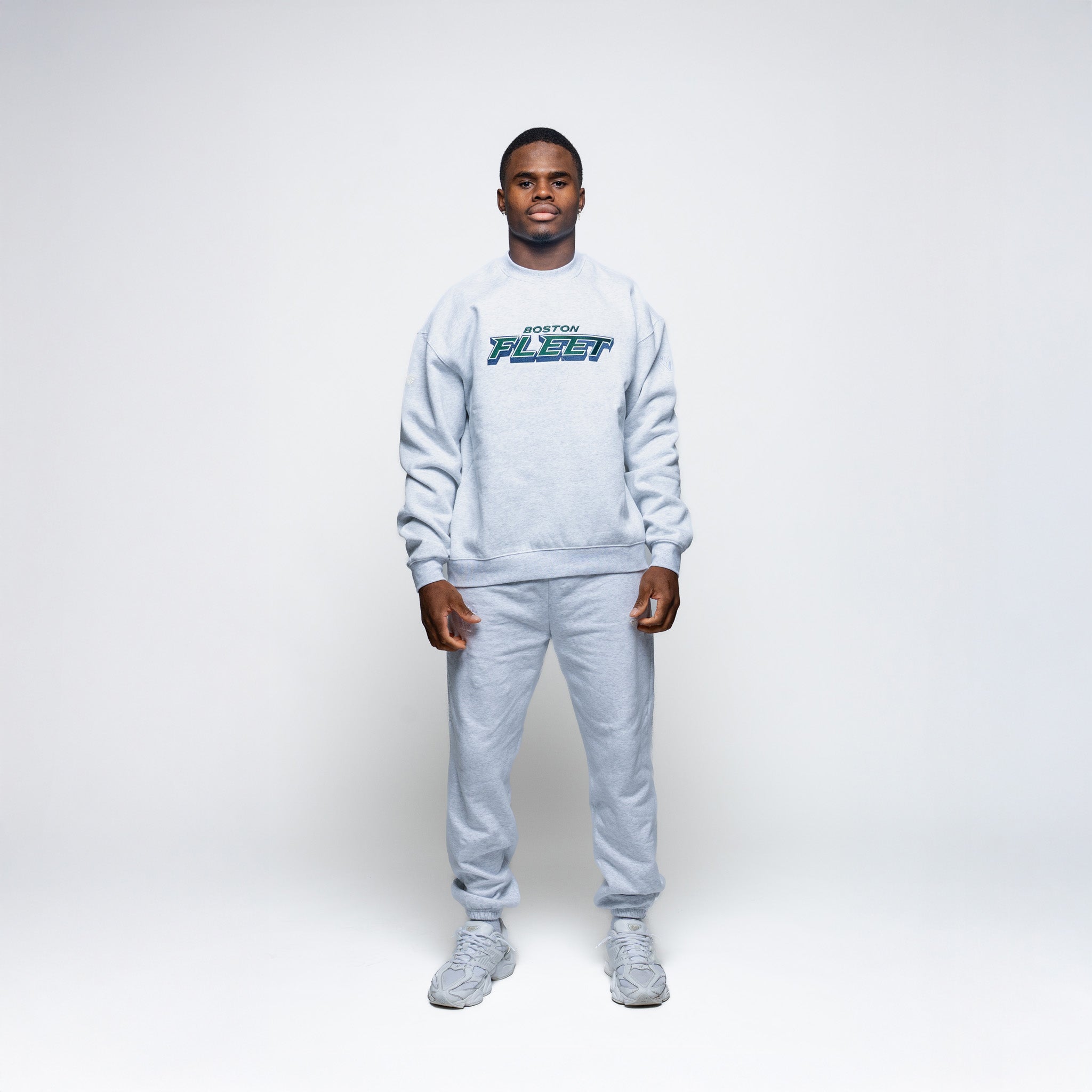 Person wearing a gray sweatshirt and pants set with 'Boston Fleet' logo on a white background