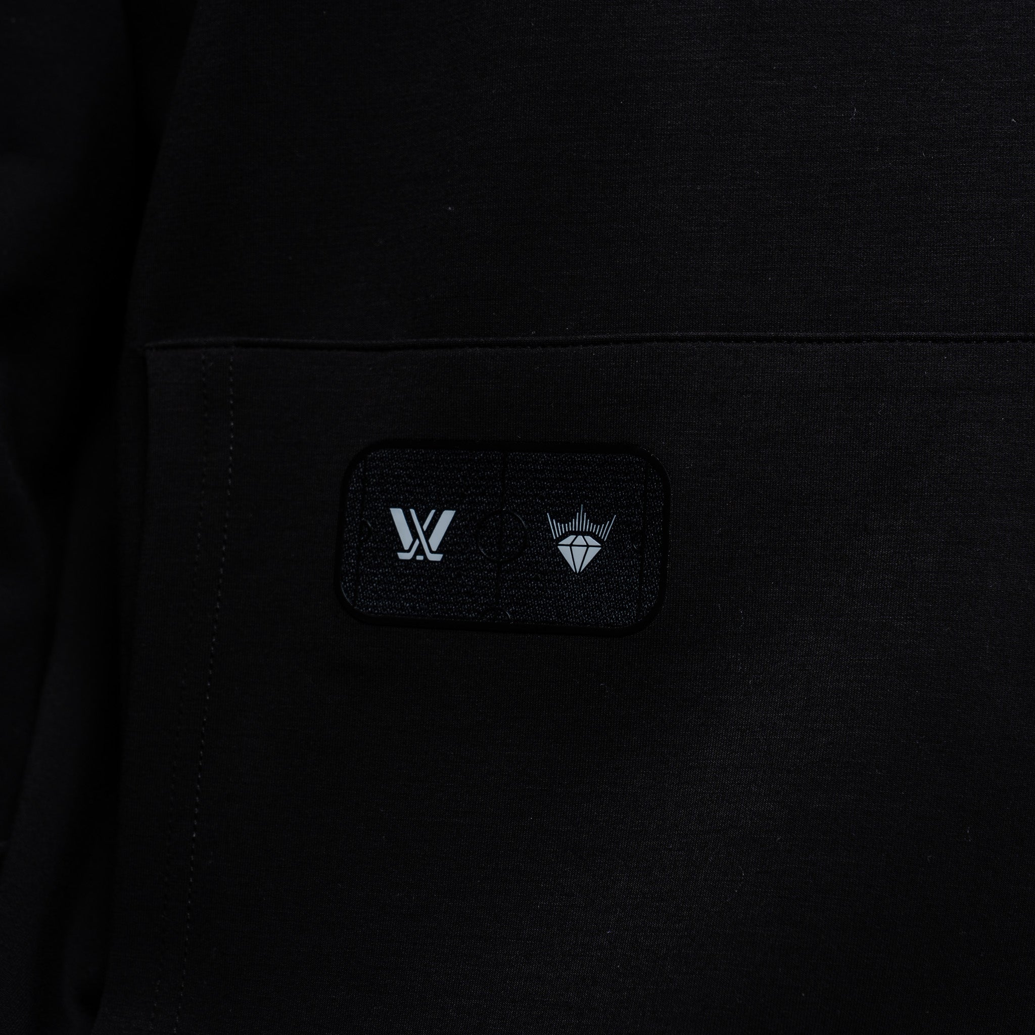 Close-up of a black hoodie with a logo patch on a dark background