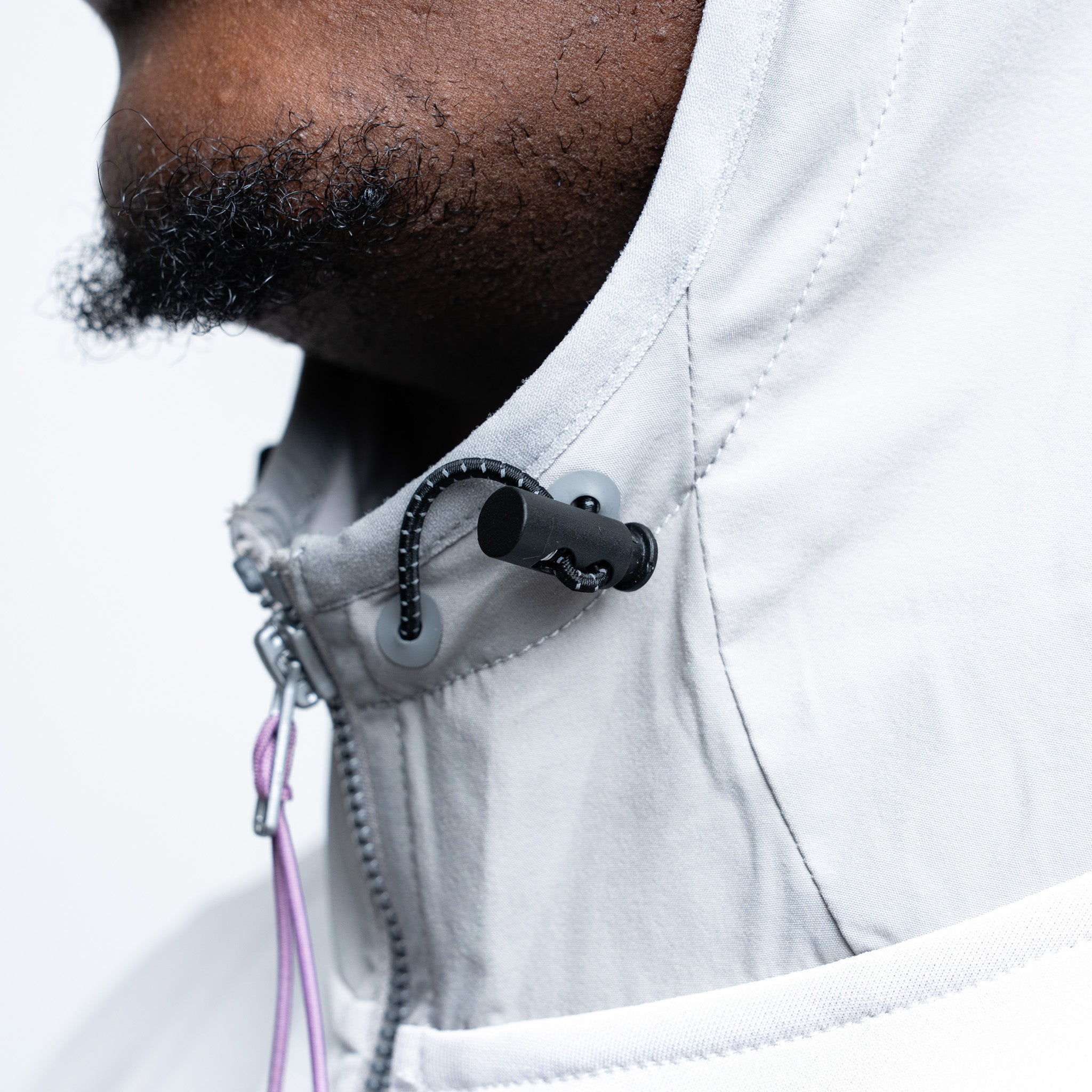 Person wearing a gray jacket with a black microphone attached to the collar on a light gray background