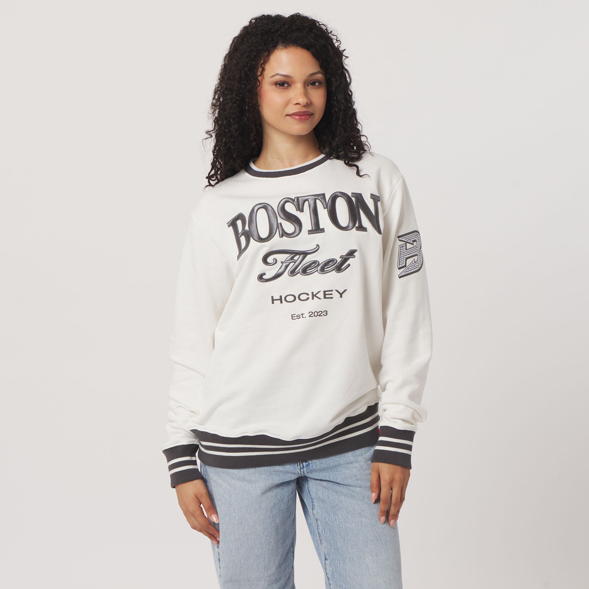 Woman wearing a white sweatshirt with 'Boston Fleet Hockey' text on a plain background