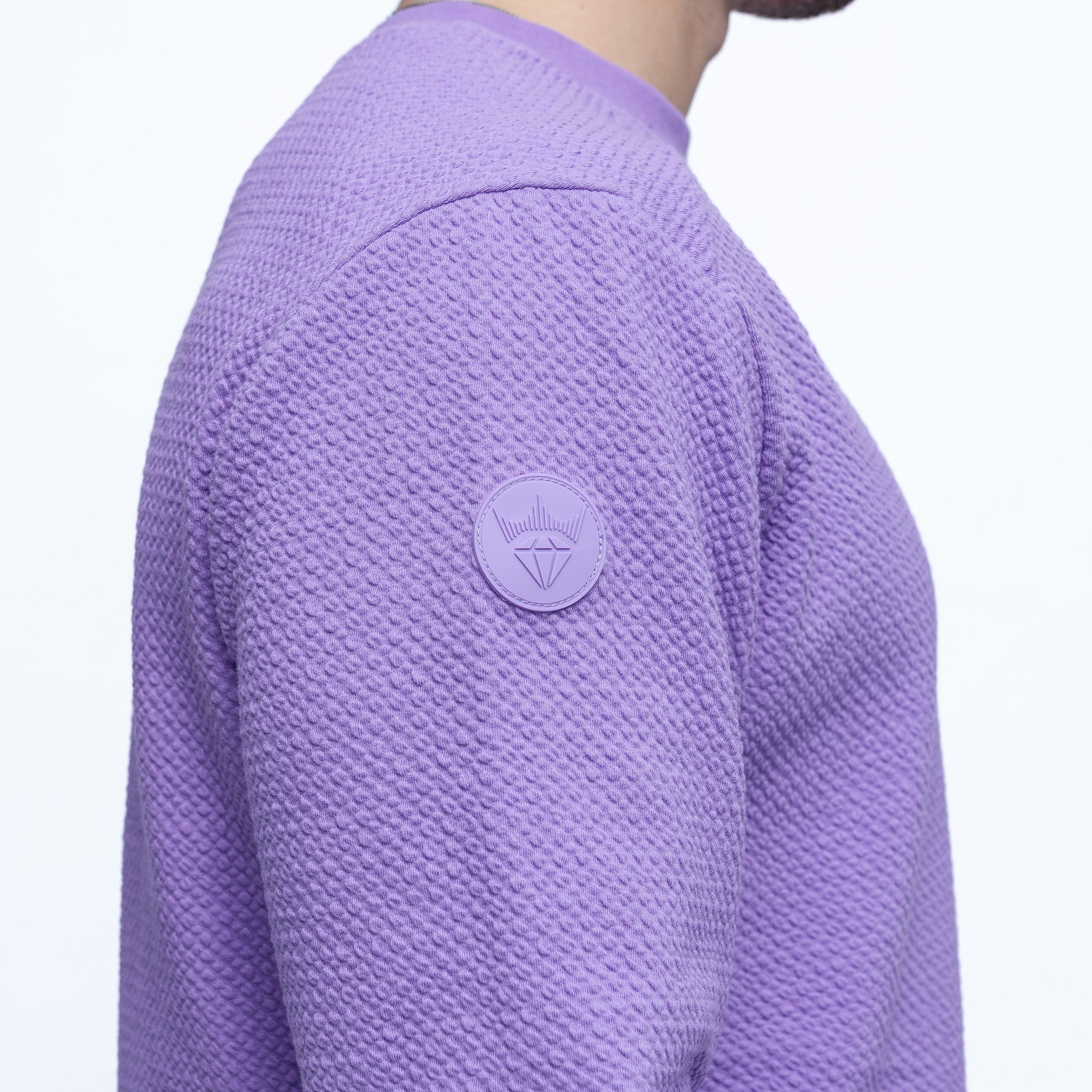 Close-up of a textured purple sweater with a brand logo on a white background
