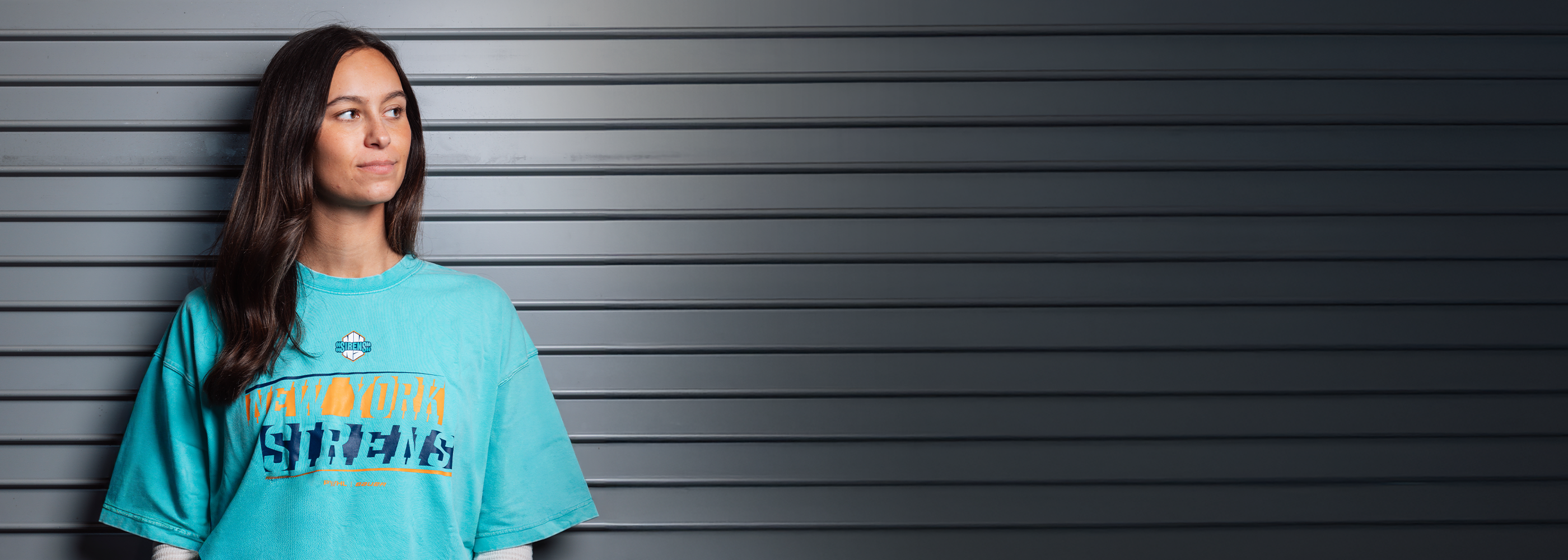 Person wearing a turquoise New York Sirens t-shirt with text against a gray background