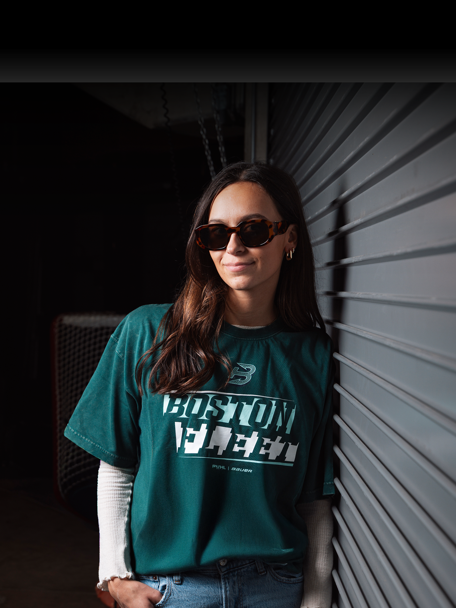 Person wearing a green Boston Fleet t-shirt with text, standing against a wall.