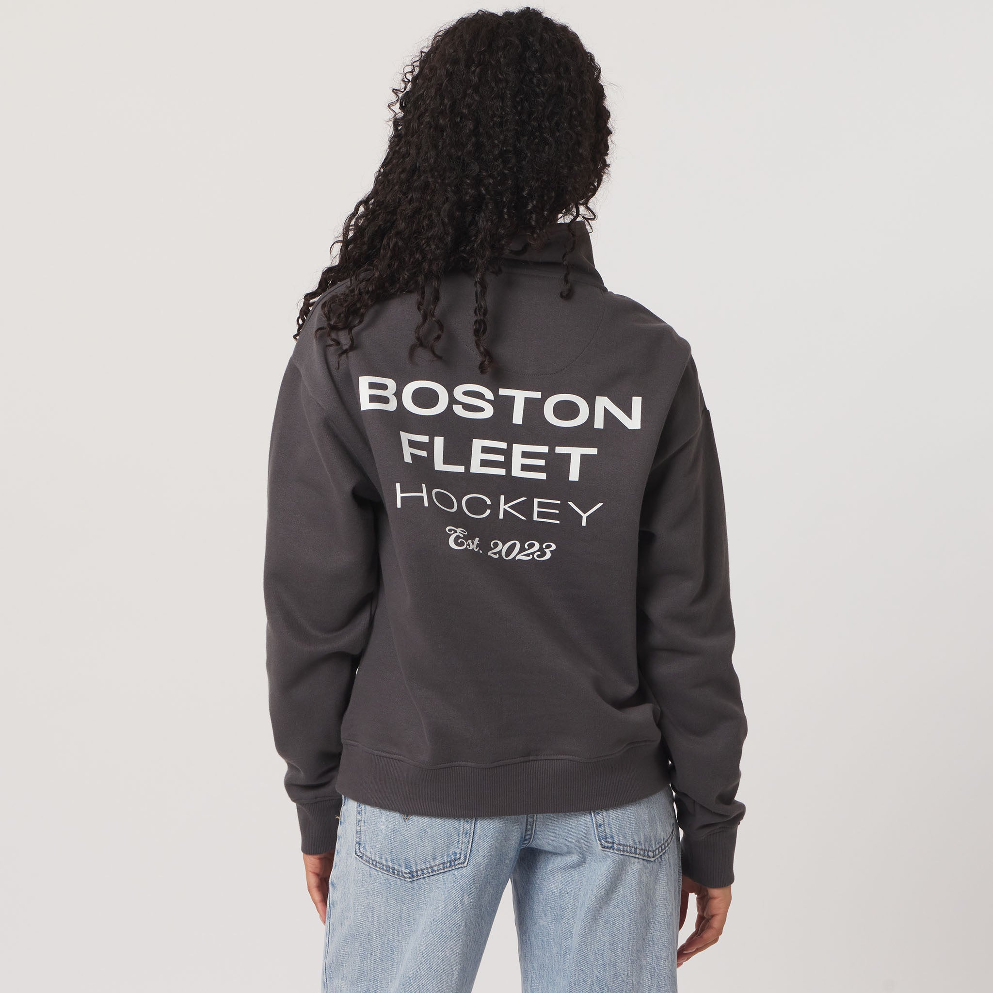 Person wearing a dark gray sweatshirt with 'Boston Fleet Hockey' text on the back, standing against a plain background.