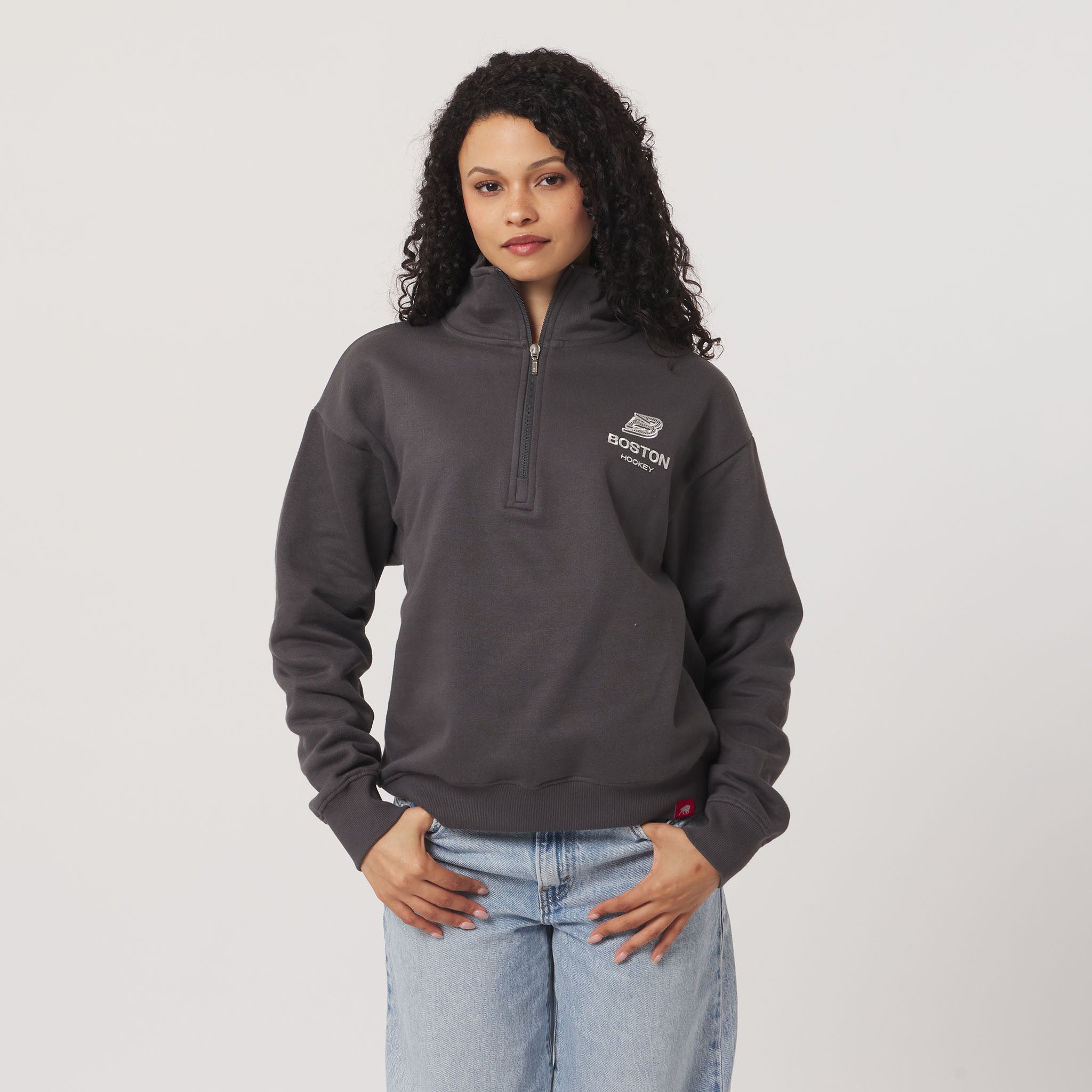 Woman wearing a gray pullover with a logo on a plain background