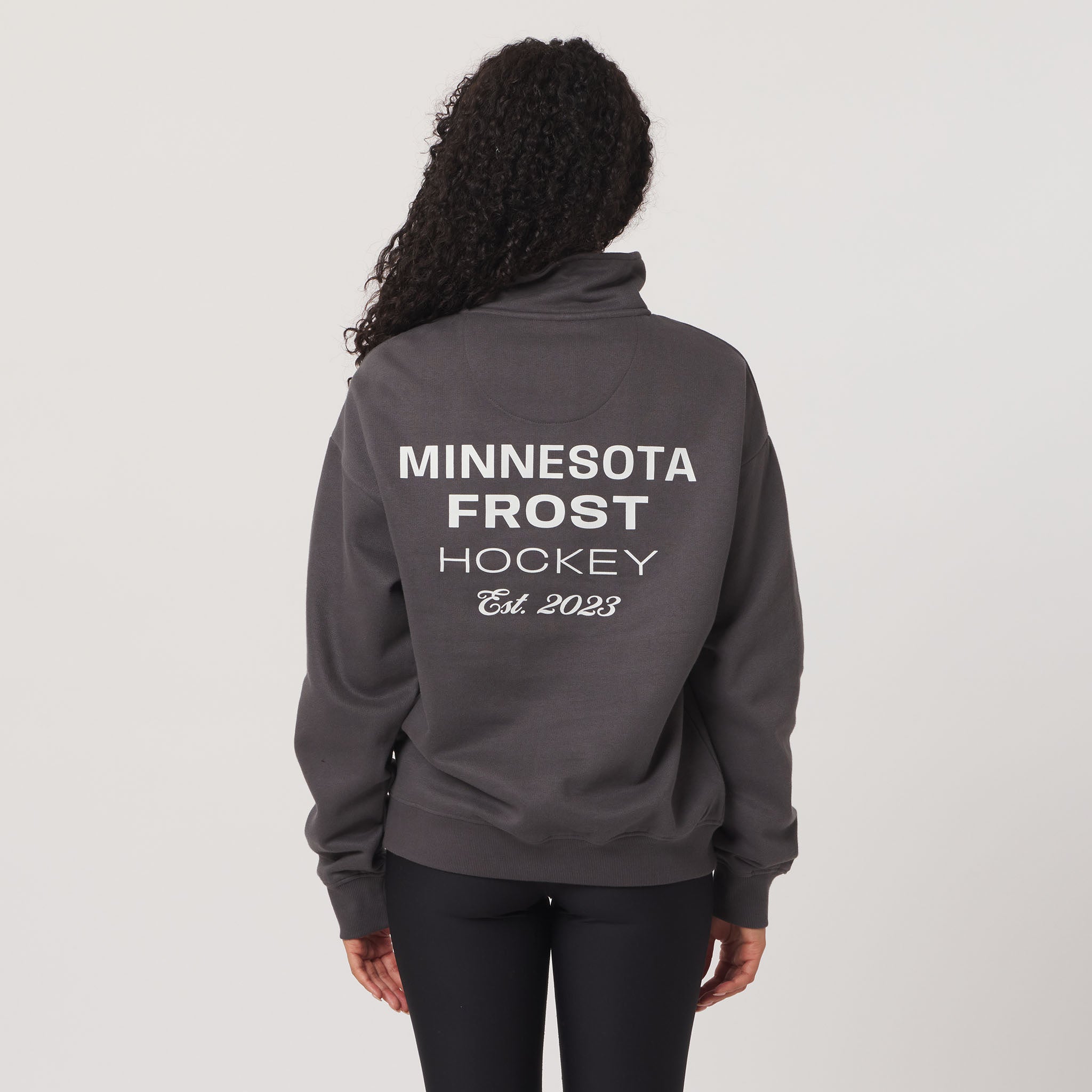 Person wearing a gray hoodie with 'Minnesota Frost Hockey Est. 2023' text on the back against a light gray background