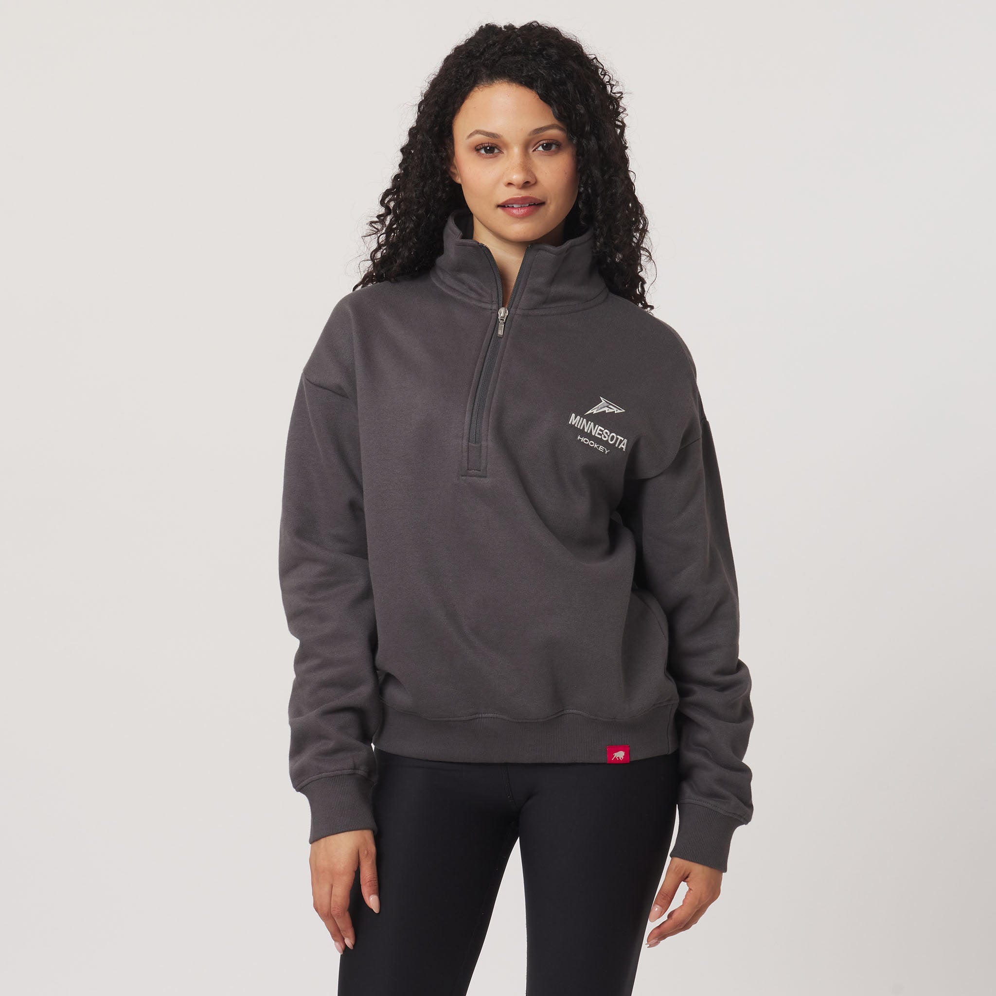 Woman wearing a gray pullover with a logo on a light gray background